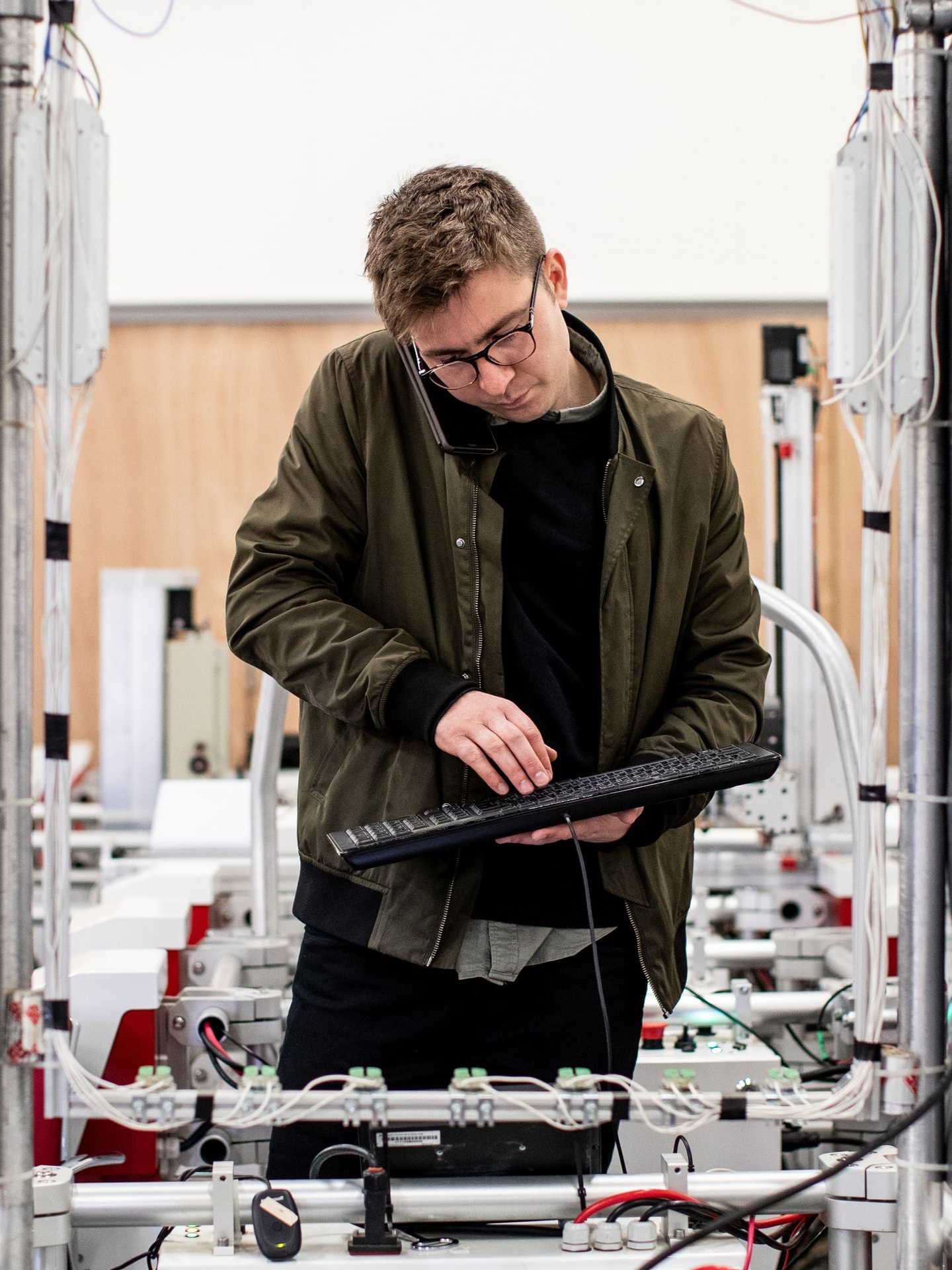 Man examining equipment in a lab, typing on a keyboard amid cables and machinery.