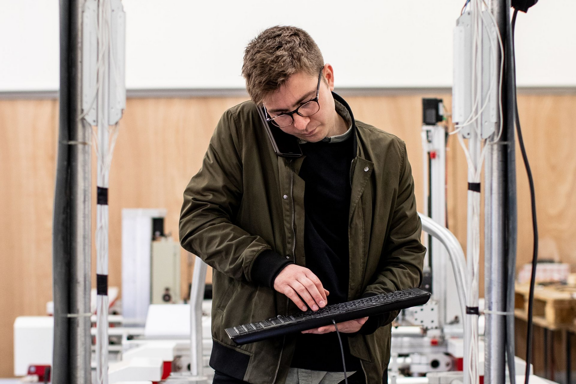 Person in a workshop adjusting equipment at a workbench, surrounded by cables and machinery.