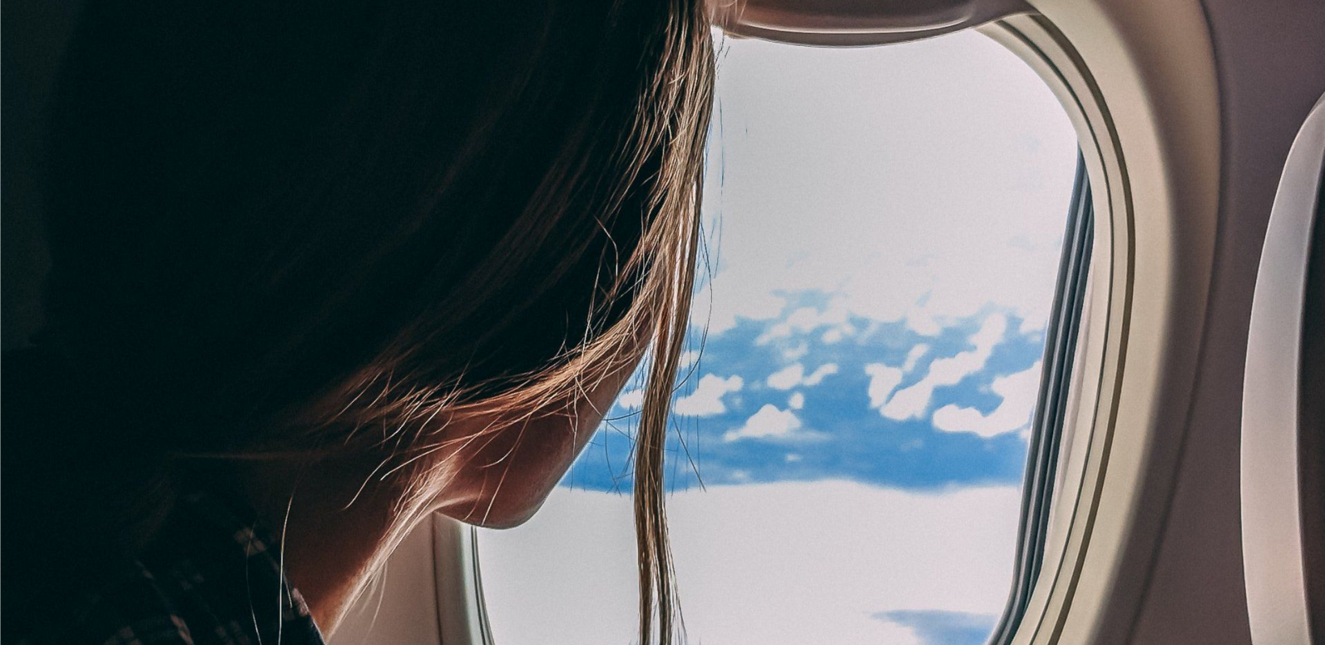 Passenger looking out an airplane window at blue sky and clouds