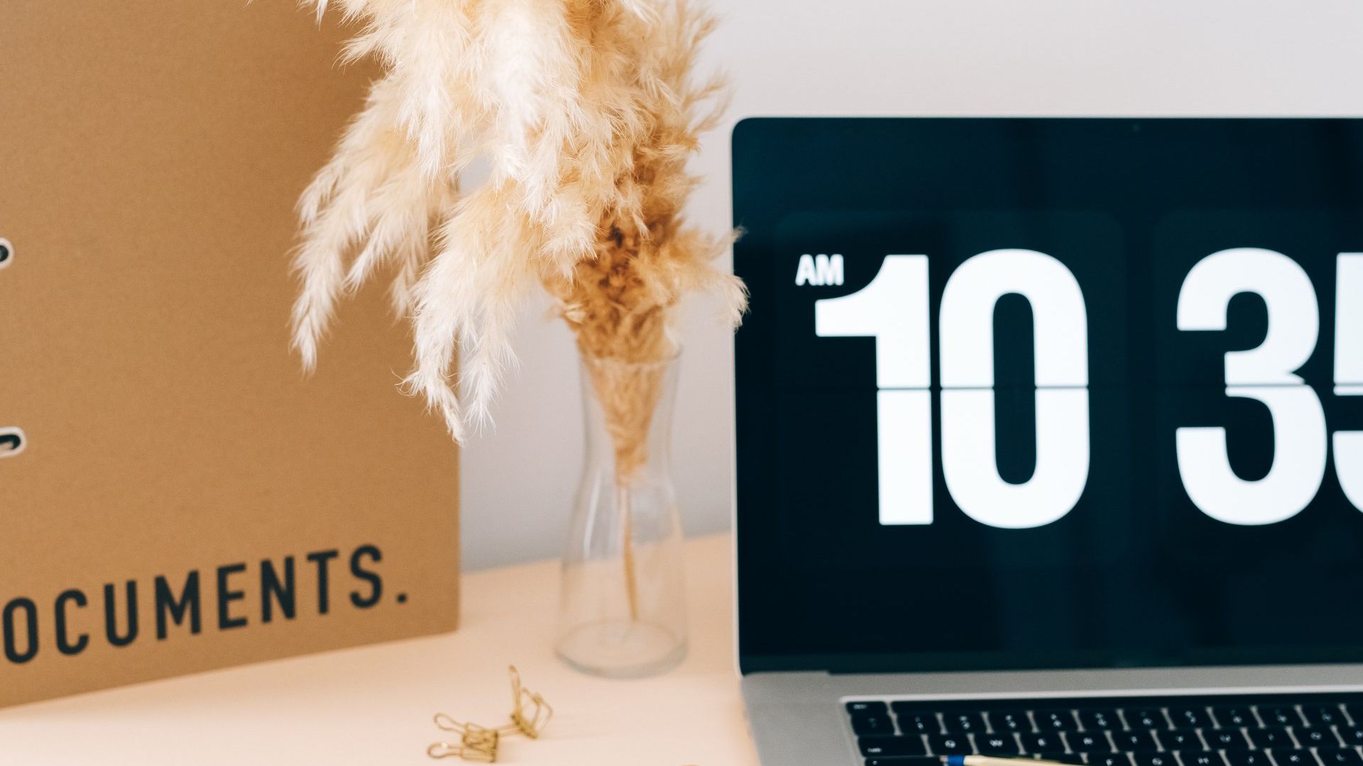 Desktop with paper documents, dried flowers in a vase, and a laptop showing 10:30 AM.