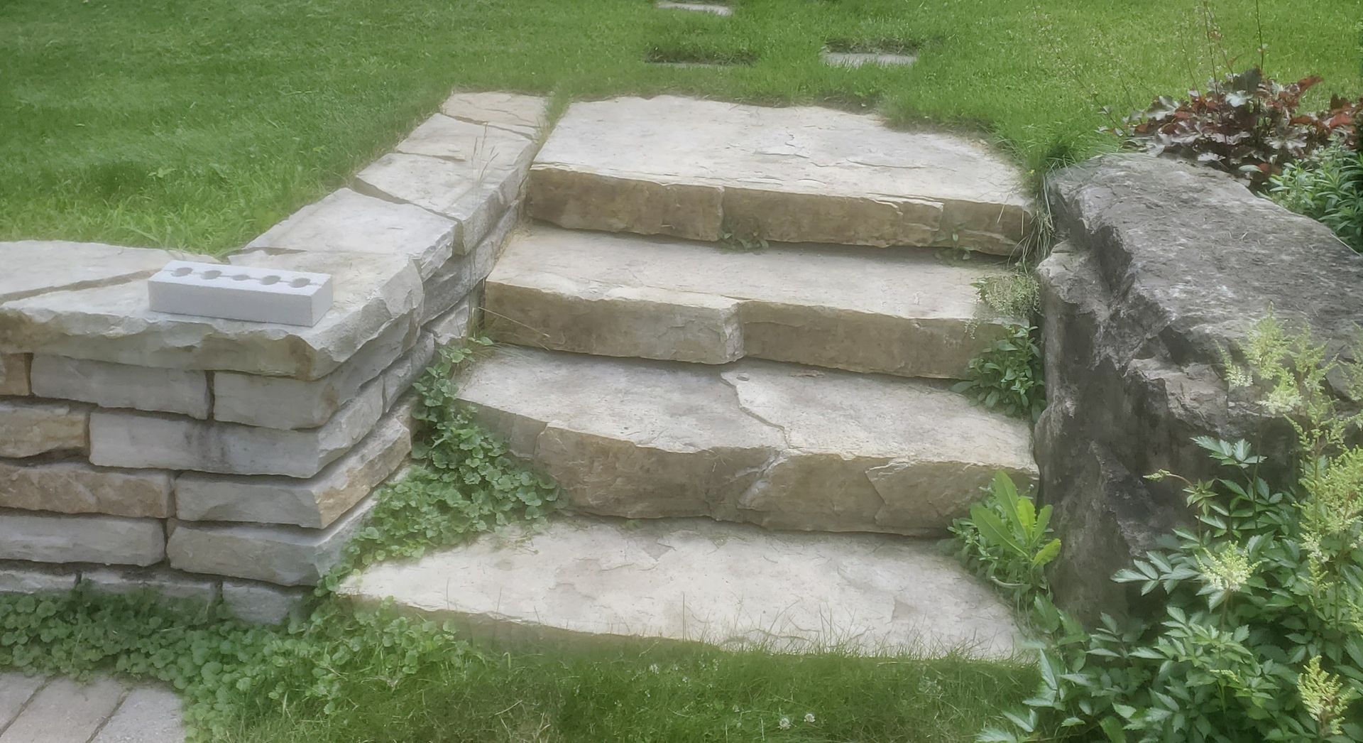 A set of stone steps leading up to a stone wall in a yard.