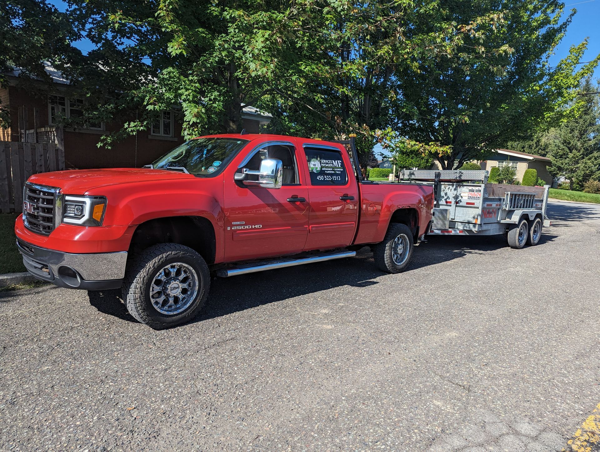 A red truck with a trailer attached to it is parked on the side of the road.