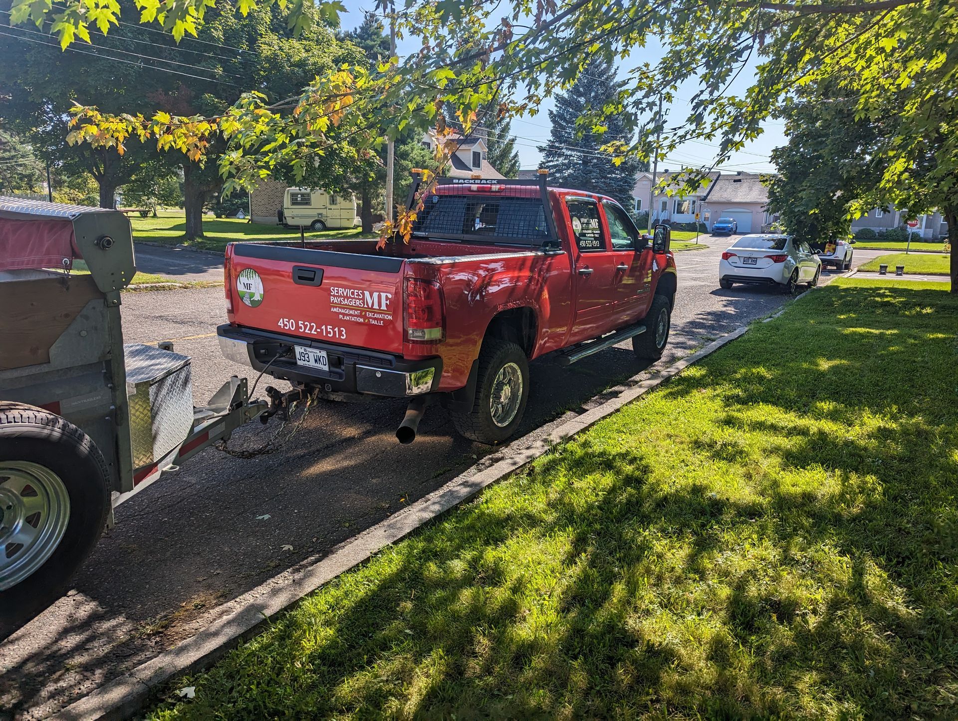 A red truck is parked on the side of the road next to a trailer.