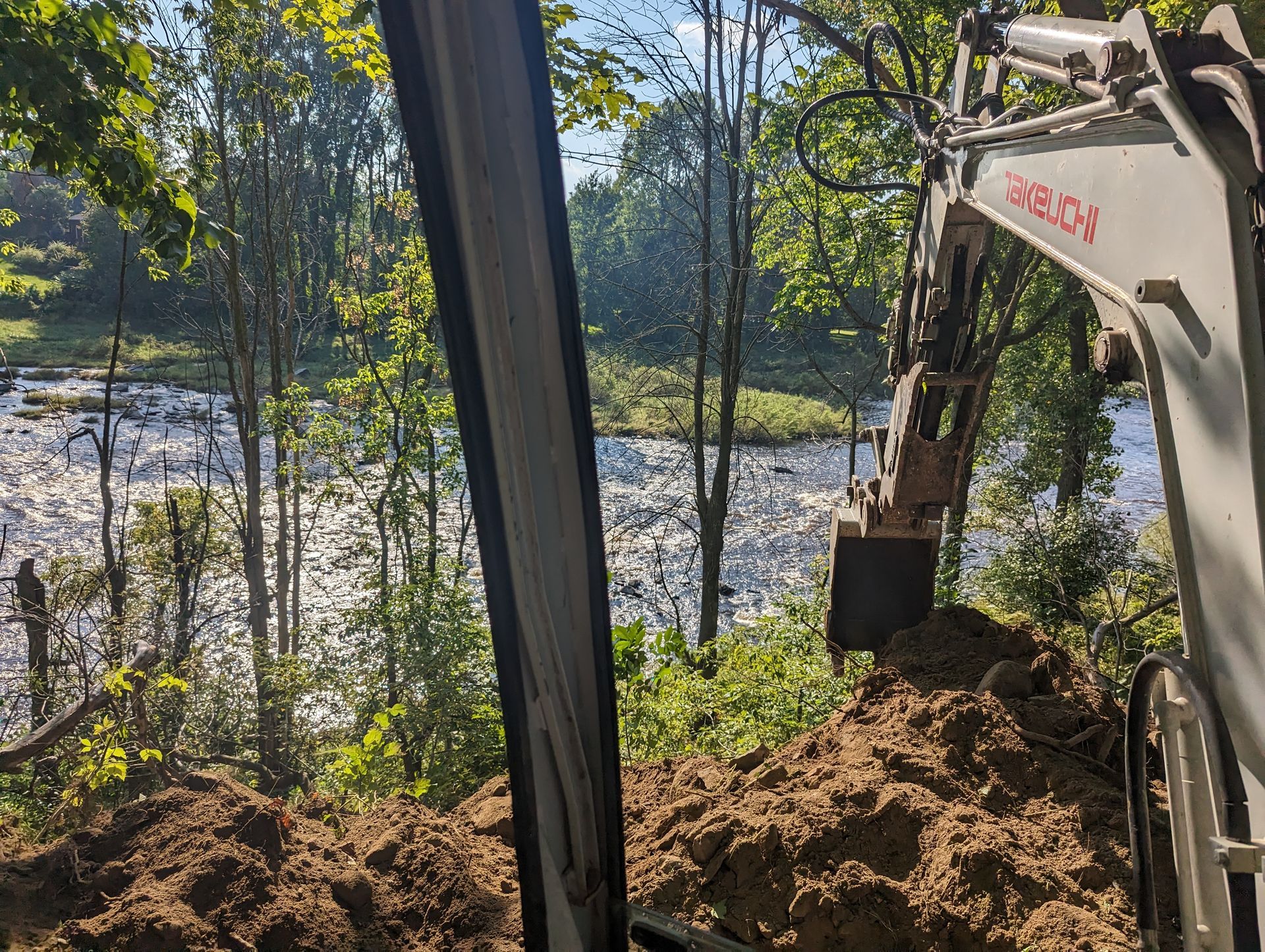 An excavator is digging a hole in the ground near a river.