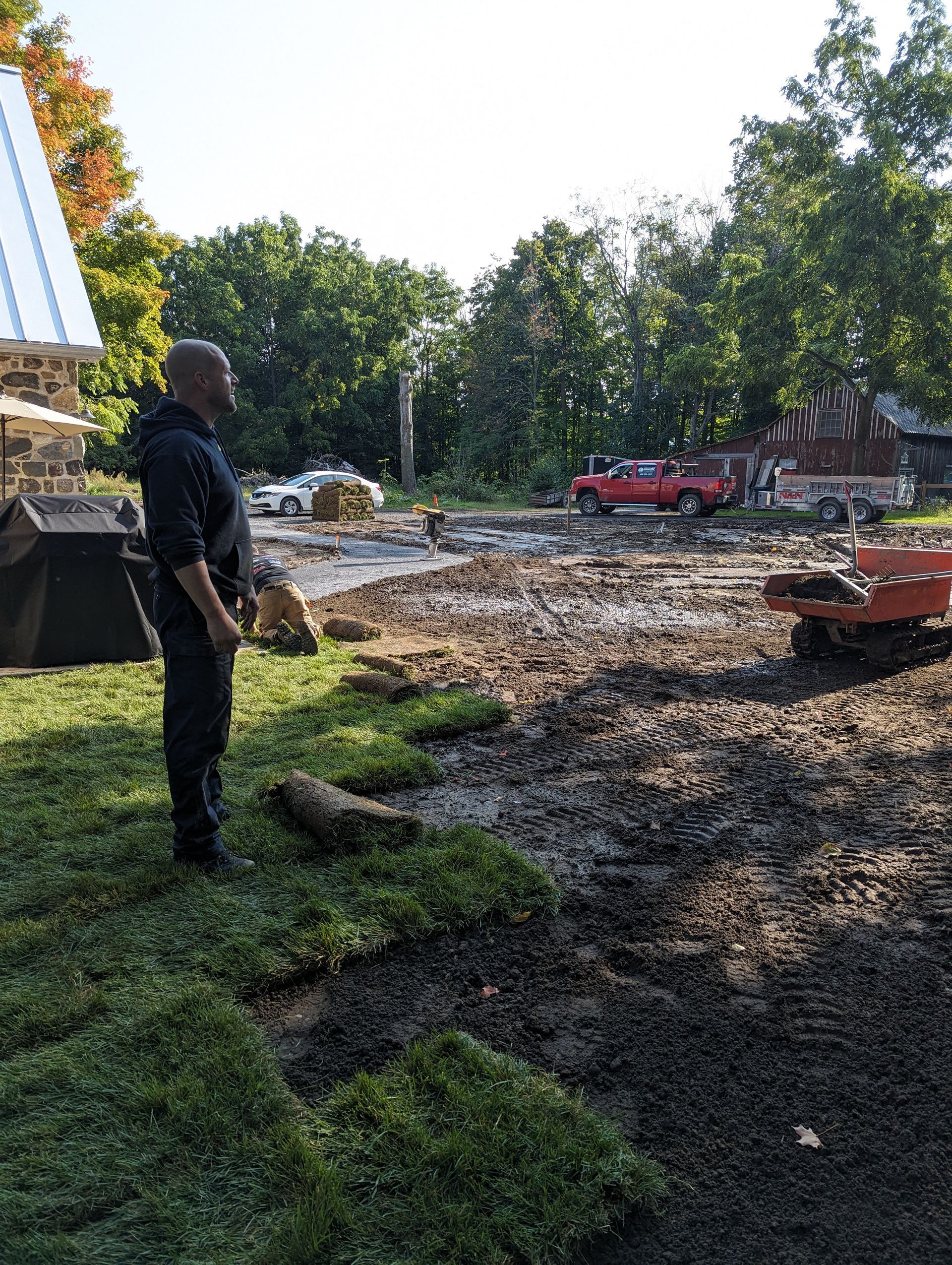 A man is standing next to a pile of grass in a dirt field.