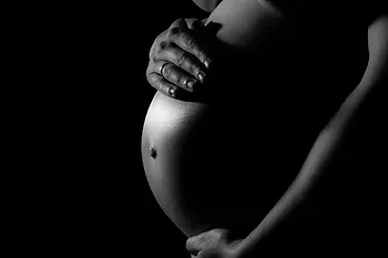 A pregnant woman is holding her belly in a black and white photo.
