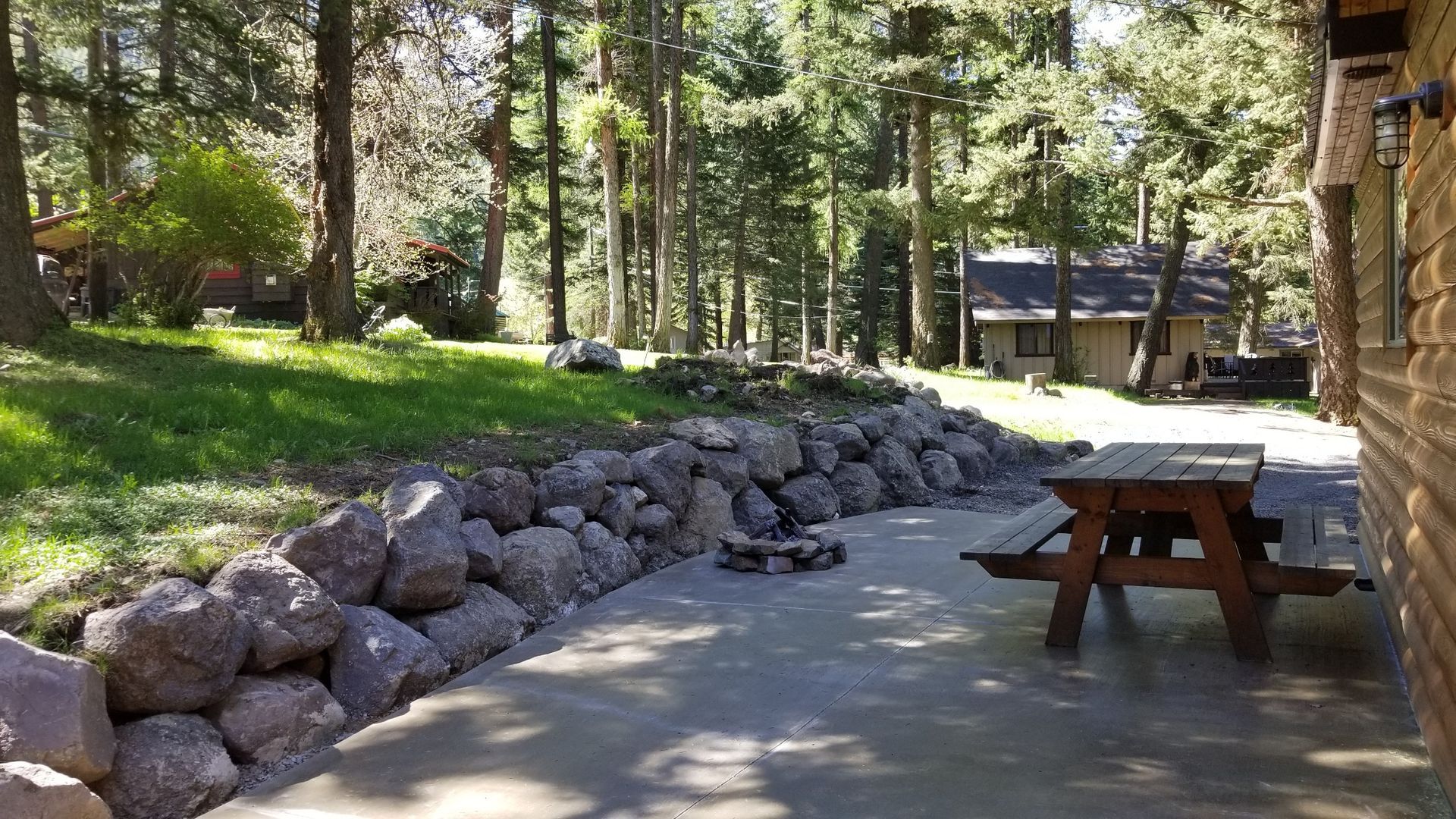A wooden picnic table is sitting on a sidewalk next to a rock wall.
