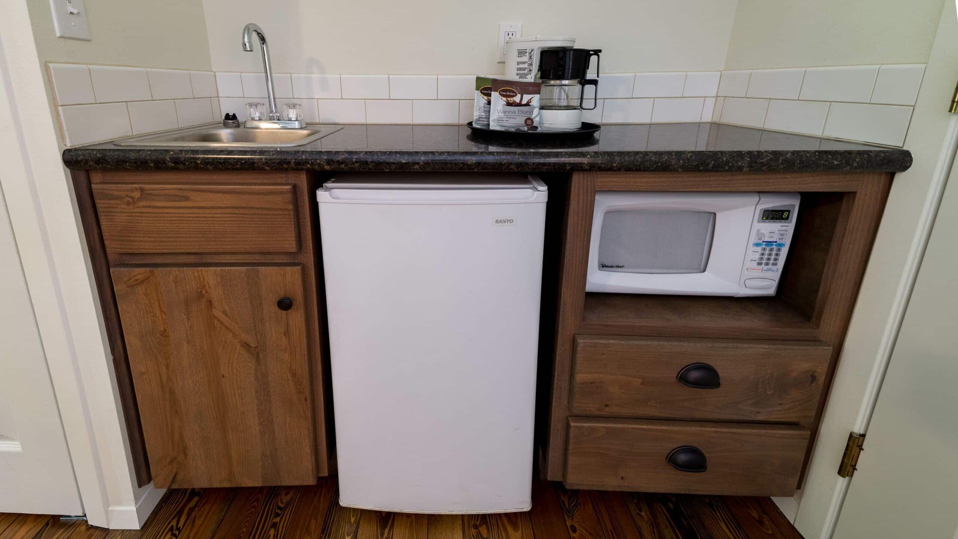 A kitchen with a sink , refrigerator , microwave and coffee maker.