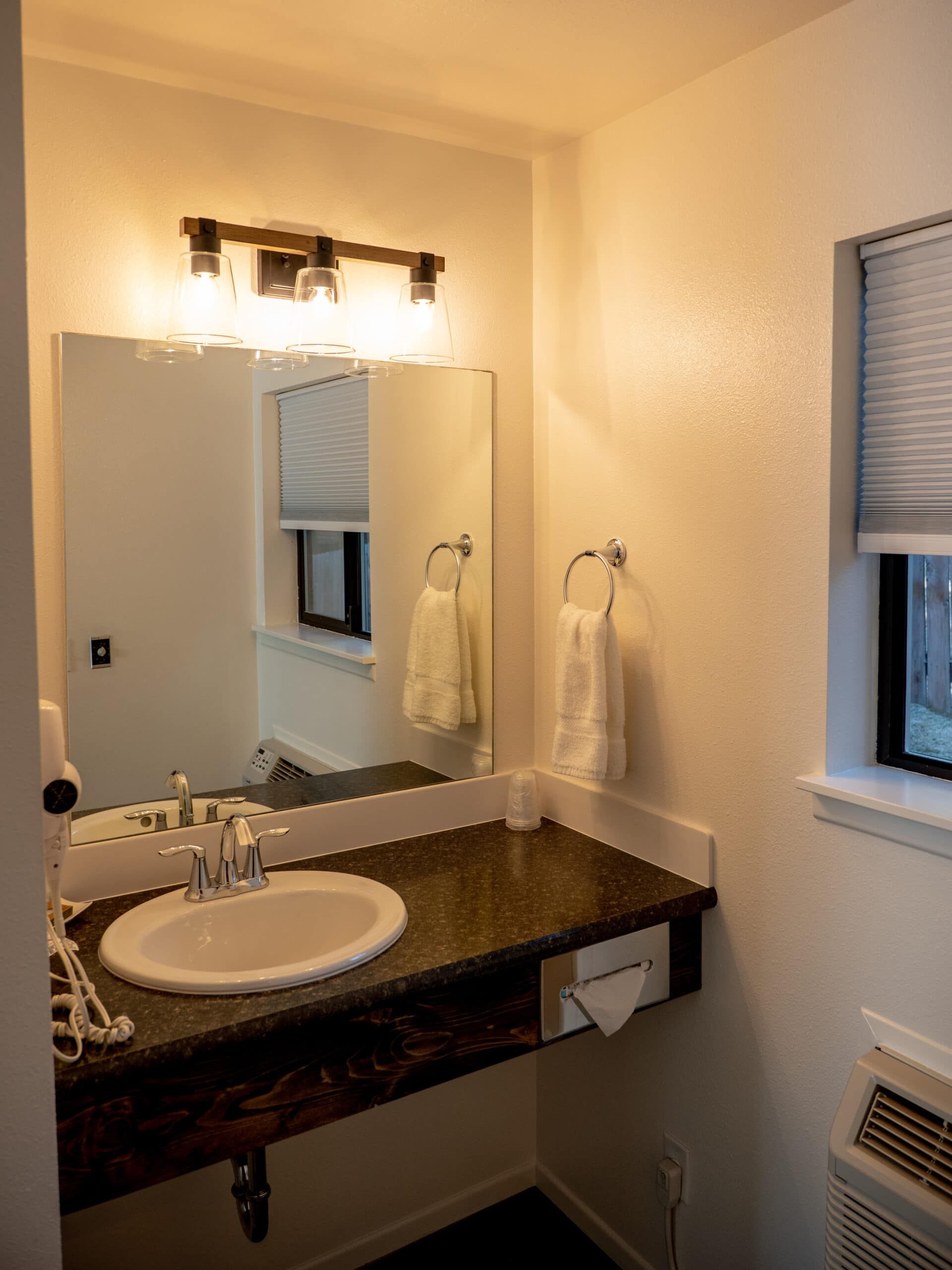 A bathroom with a sink , mirror and window.