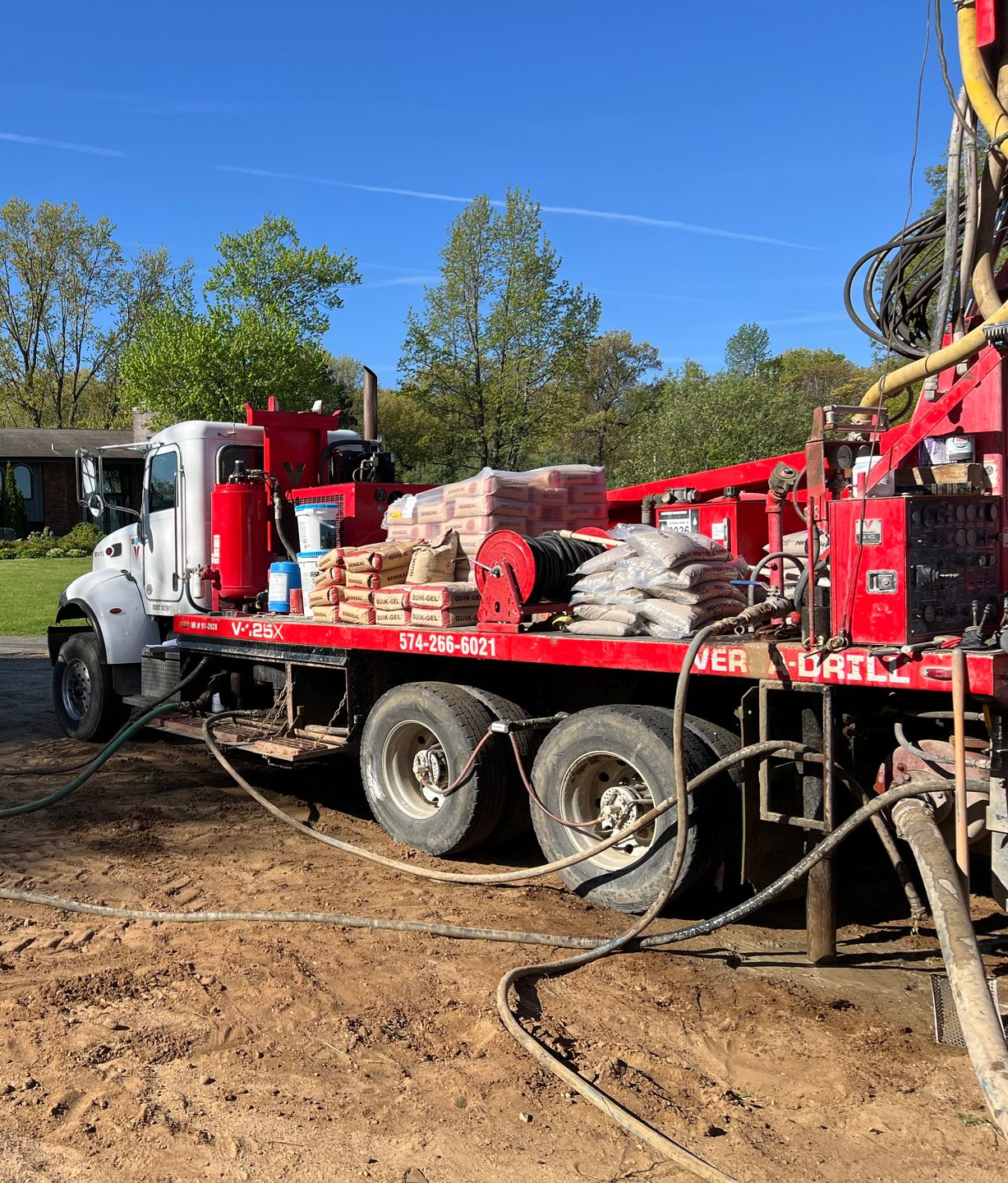 A red and white well drilling truck parked outdoors on a sunny day, with supplies loaded.