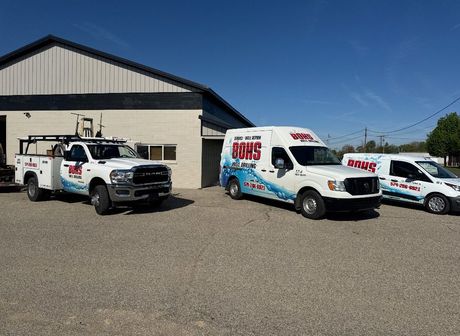 Three white service vehicles parked in front of a tan building under a blue sky.