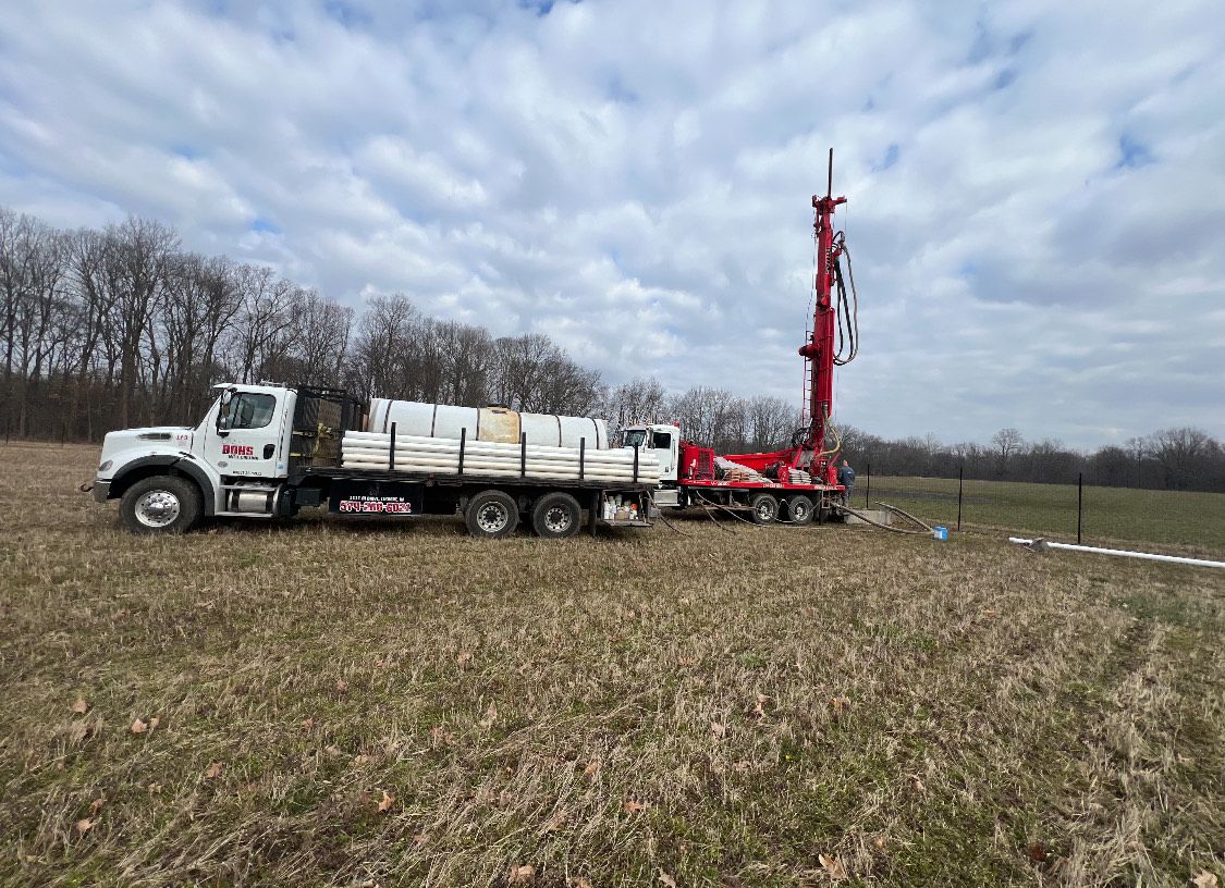 Truck and drilling rig in a field, preparing to drill. Red, white and green in a cloudy sky.