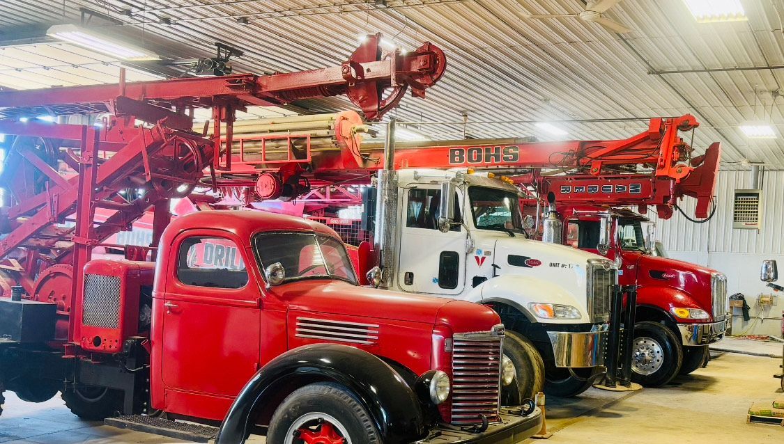 Three red oil field trucks parked inside a garage. The front truck is an older model.