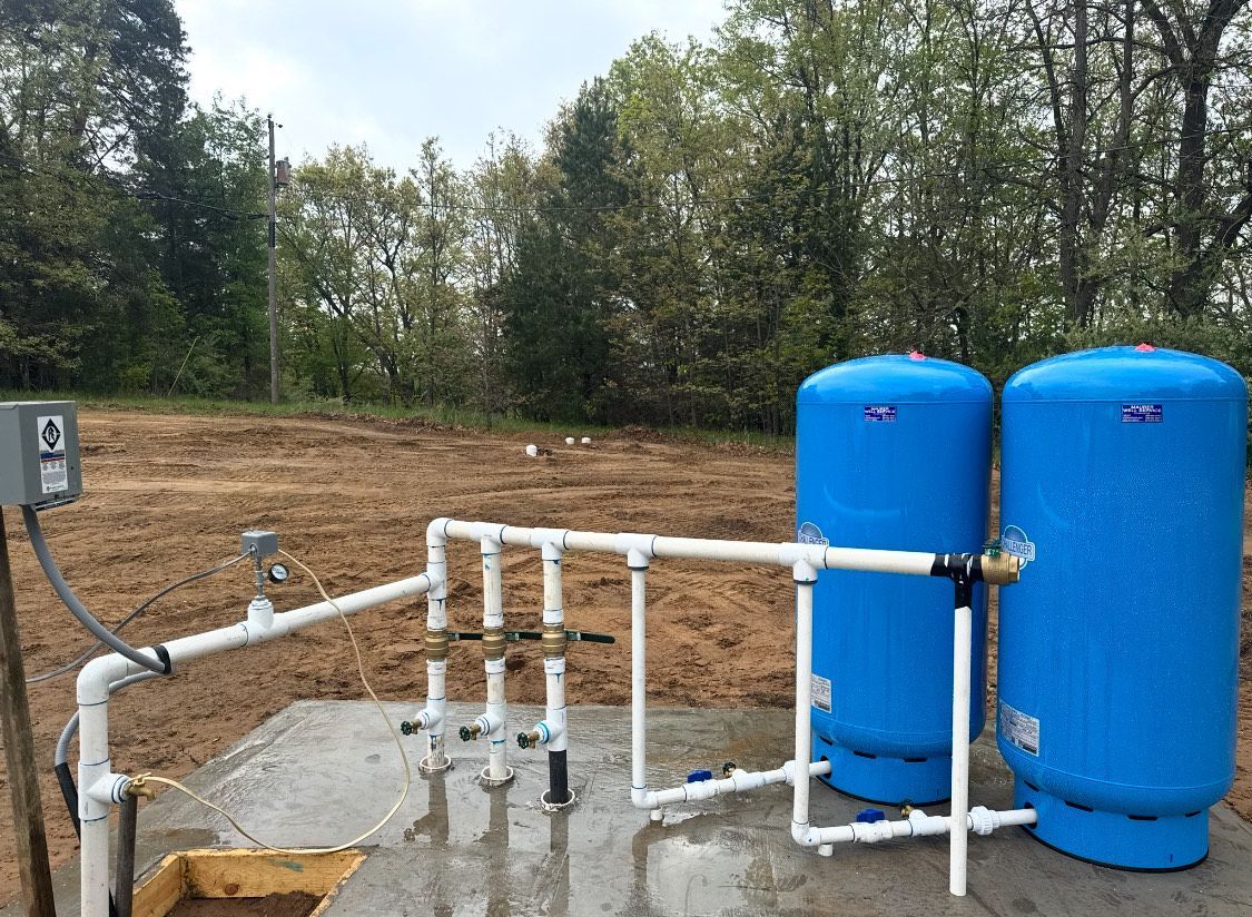 Two blue water tanks and associated pipes on a concrete pad, outdoors.