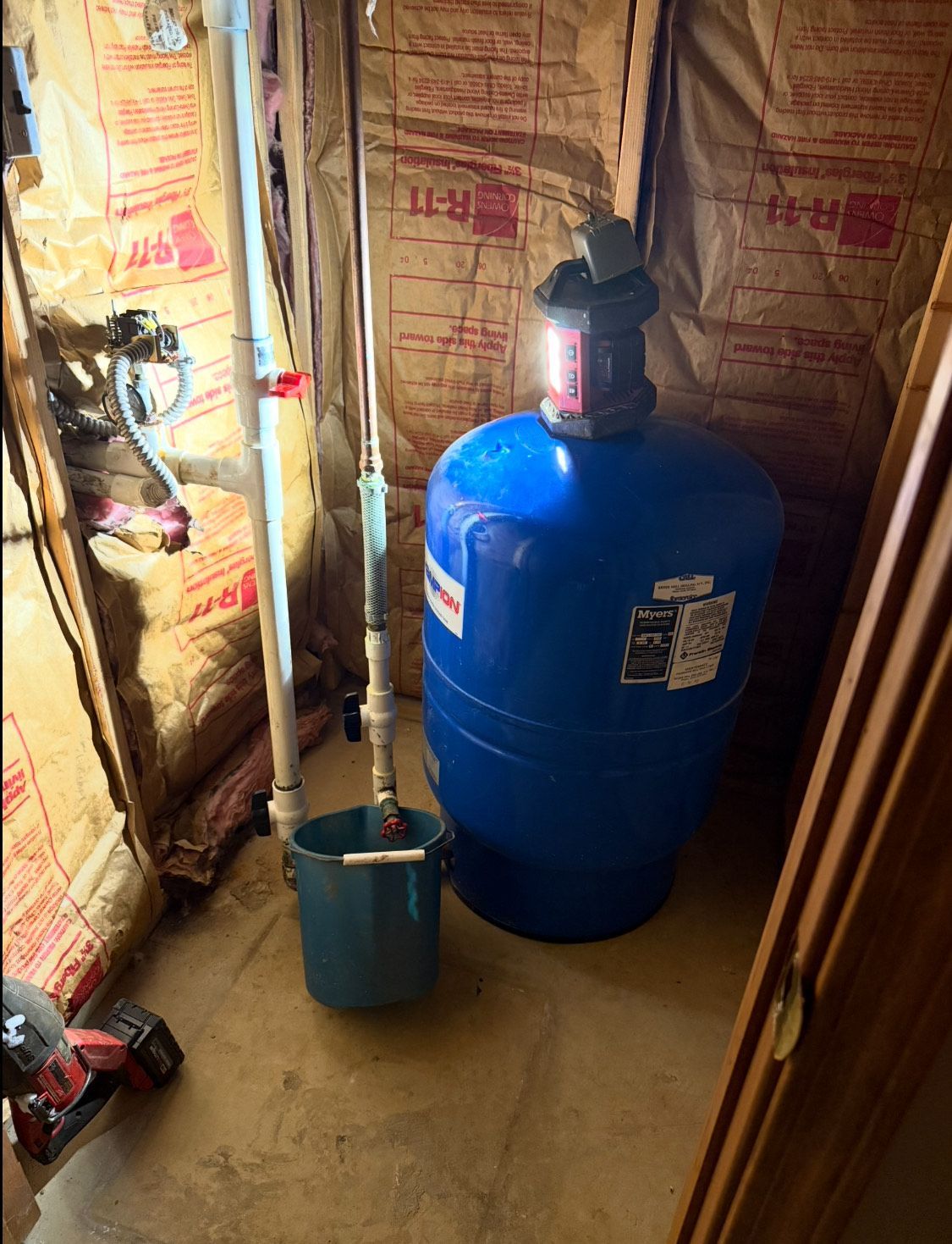 Blue water pressure tank, bucket, pipes in unfinished basement.