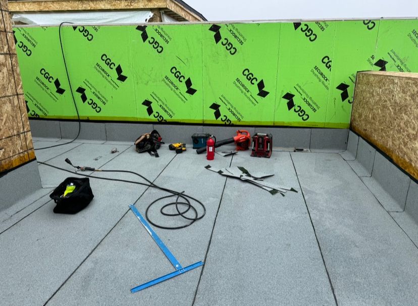 Construction tools scattered on a rooftop deck beside a green insulated wall.