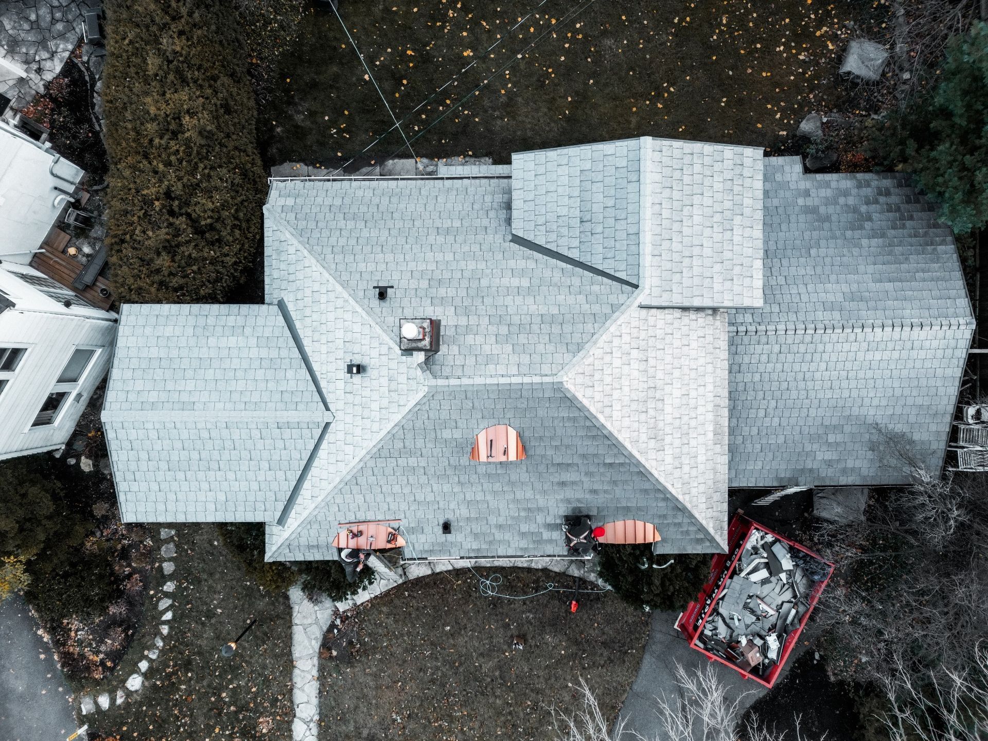 Aerial view of a gray-shingled house with a large roof, surrounded by trees and yard debris.