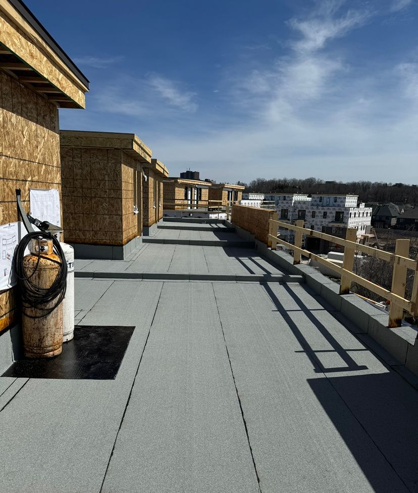Rooftop walkway with wooden walls, gray decking, and a blue sky overlooking buildings.
