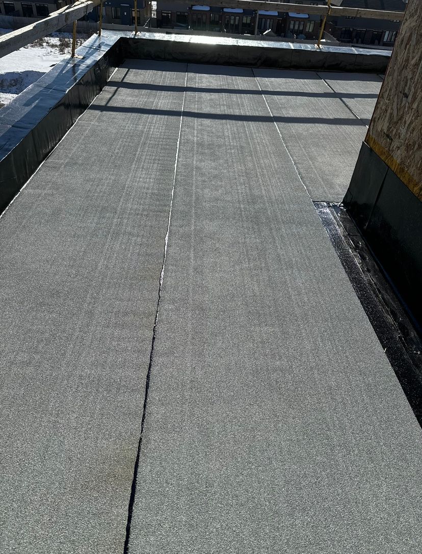 Flat gray rooftop with a central seam and low black parapet walls in bright sunlight