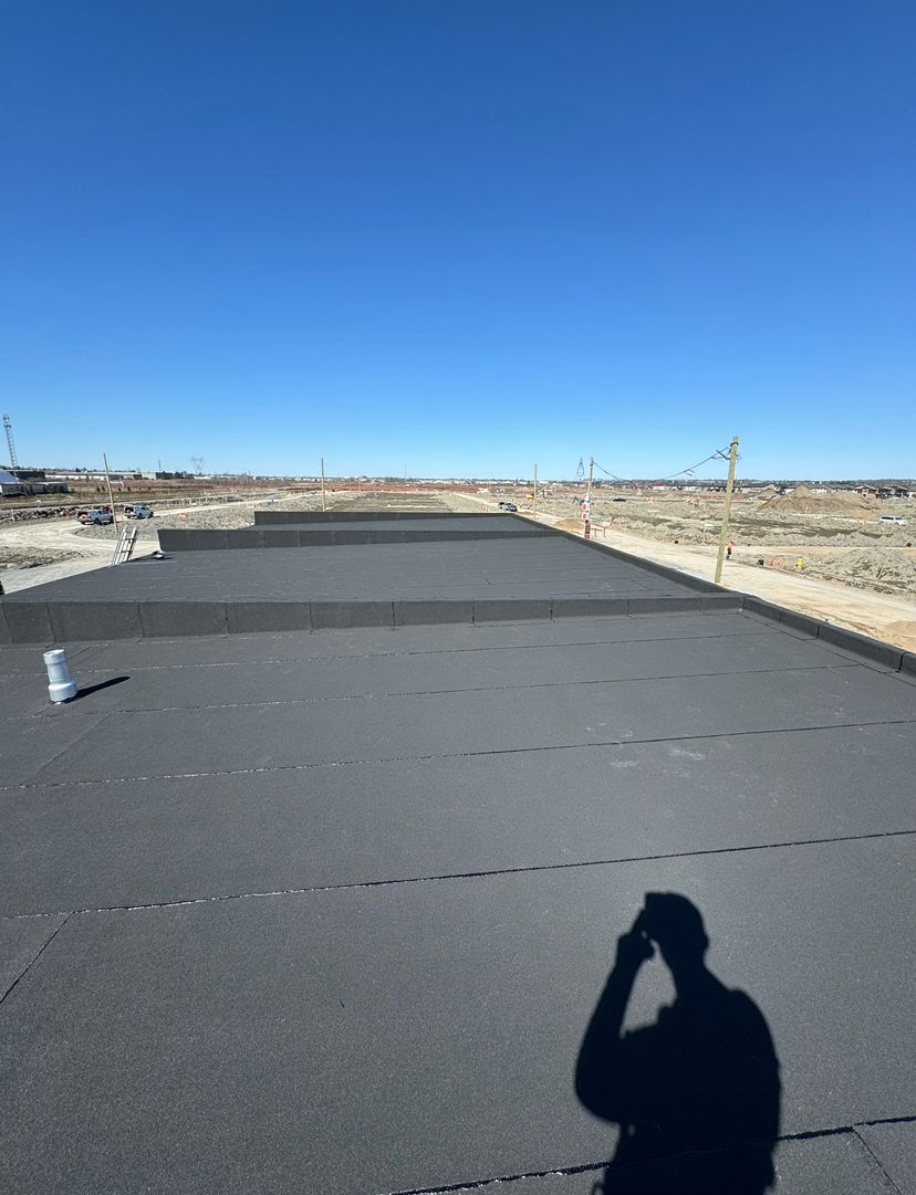 Empty paved road under a clear blue sky in a dry, open landscape, with a person’s shadow in the foreground