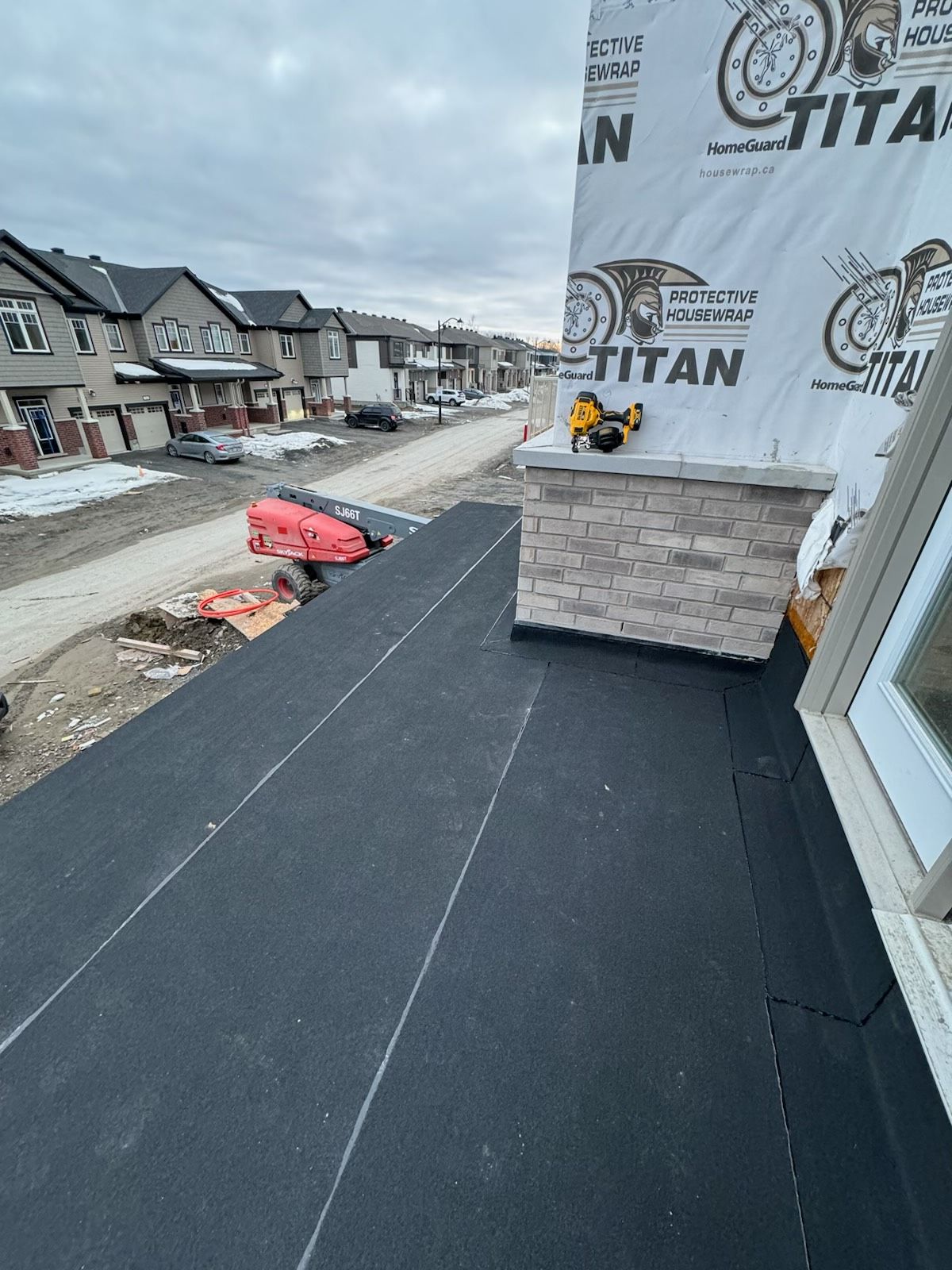 Roof under construction with black underlayment, house wrap, and snowy suburban homes in the background