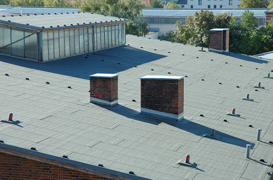 Rooftop with gray shingles, two brick chimneys, and a glass skylight under a clear sky