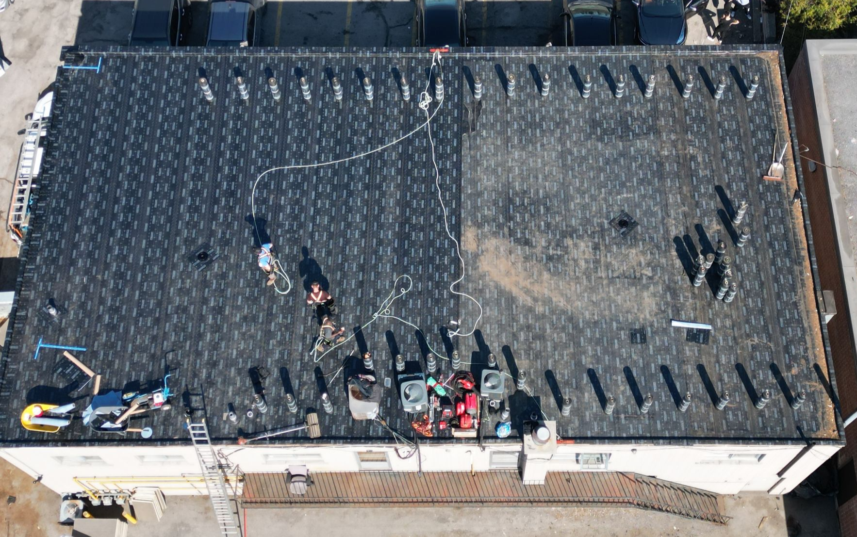 Rooftop with black tar surface, a white hose across it, and tools/equipment near the lower edge.