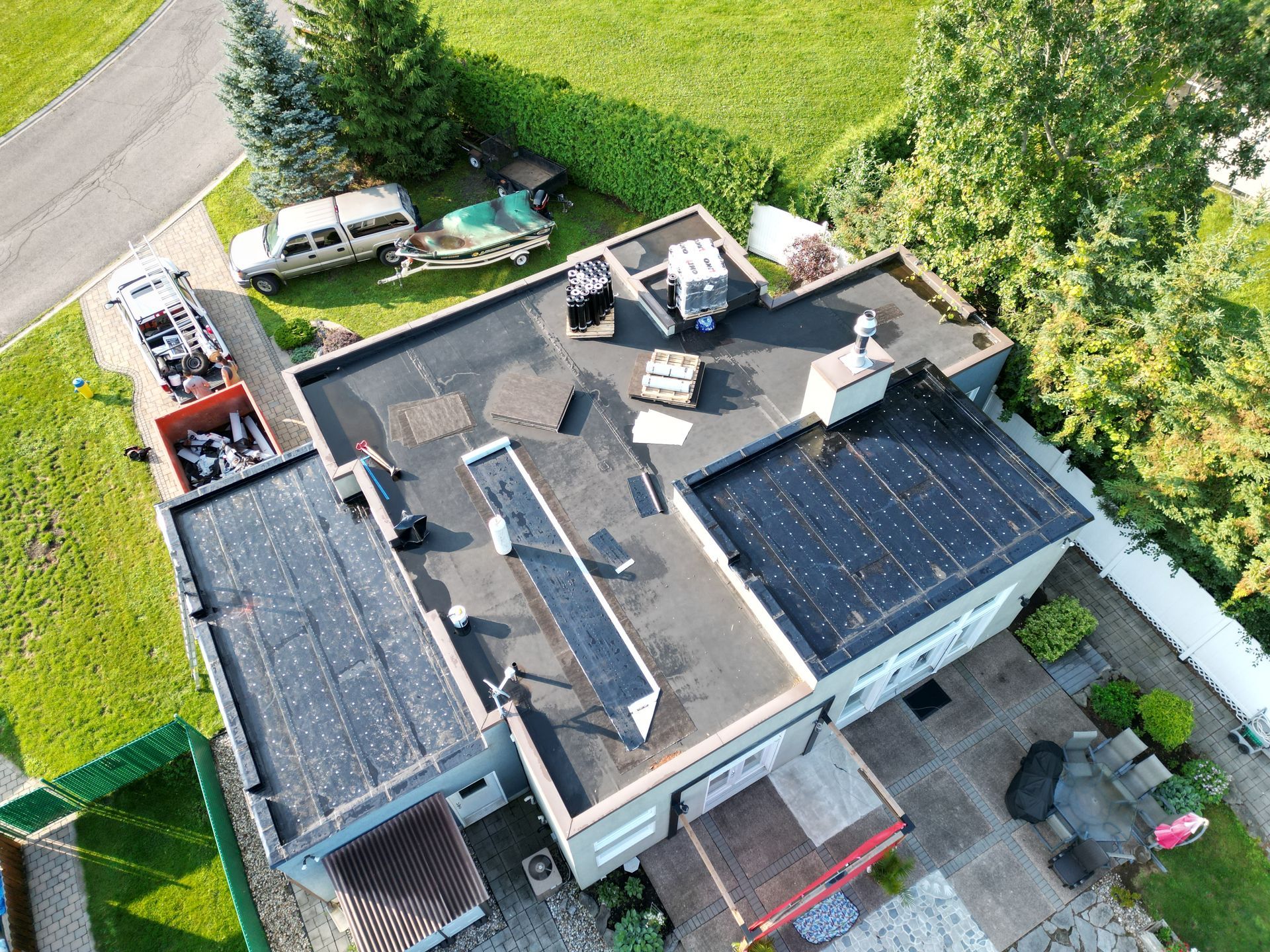 Aerial view of a house roof with solar panels, patio furniture, and green yard surrounding it.