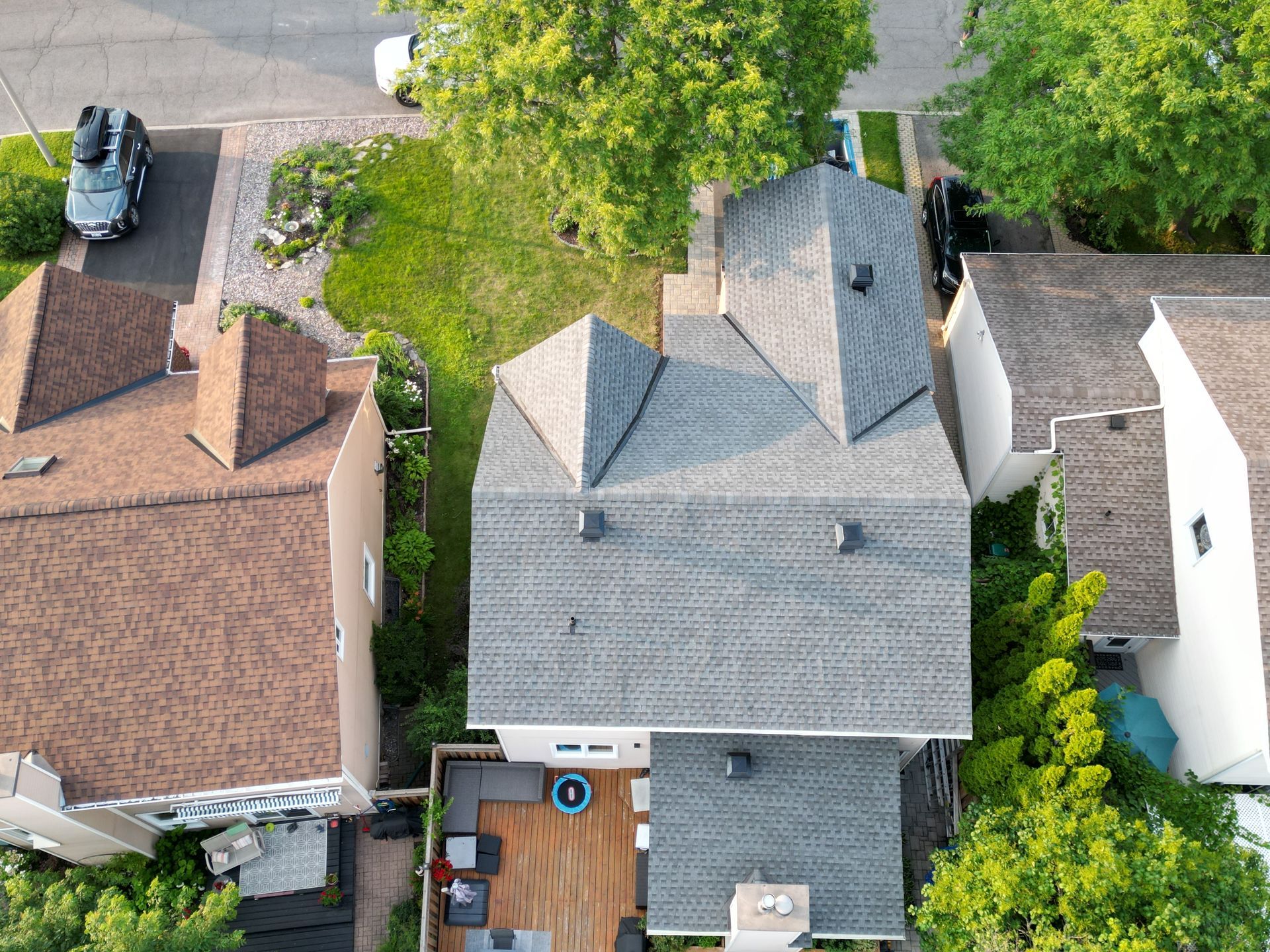 Aerial view of three suburban houses with trees, driveways, and a parked car on the street.