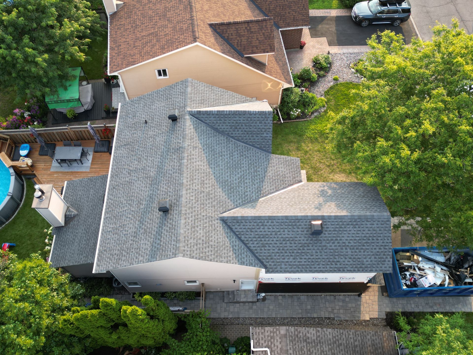Aerial view of a house with gray roof, surrounded by trees and neighboring homes.