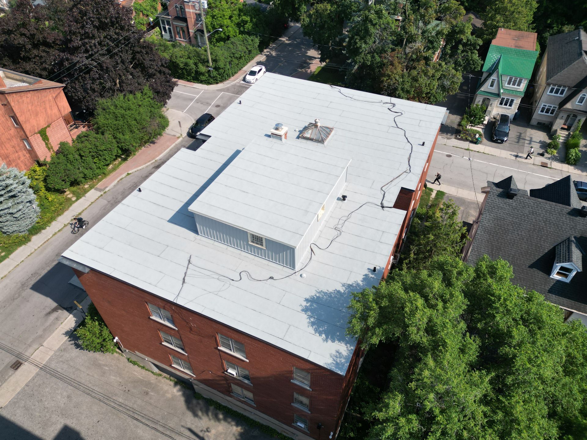 Aerial view of a red-brick building with a white roof on a tree-lined street