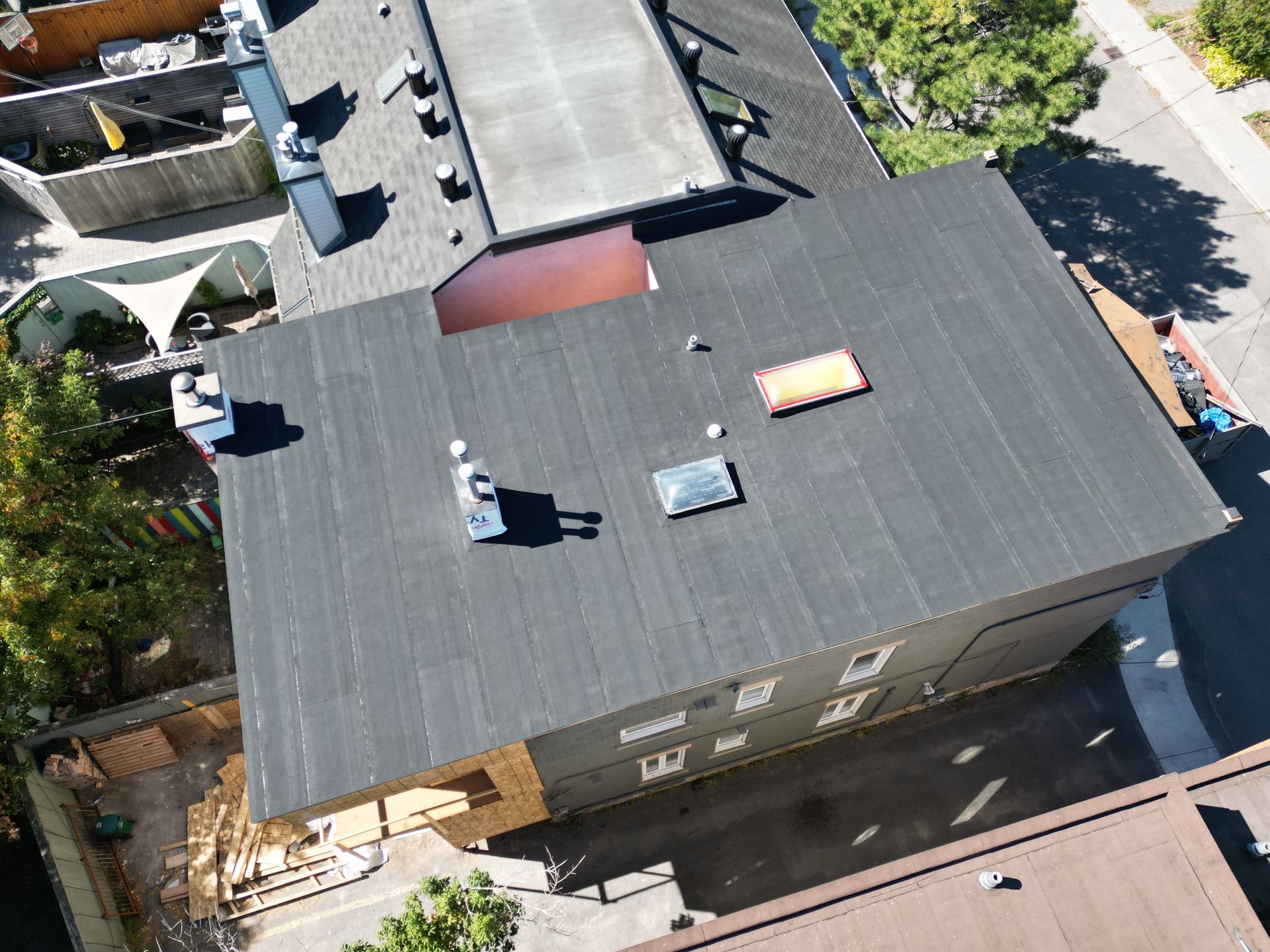 Aerial view of a gray-roofed building with rooftop vents and skylights beside a street and trees