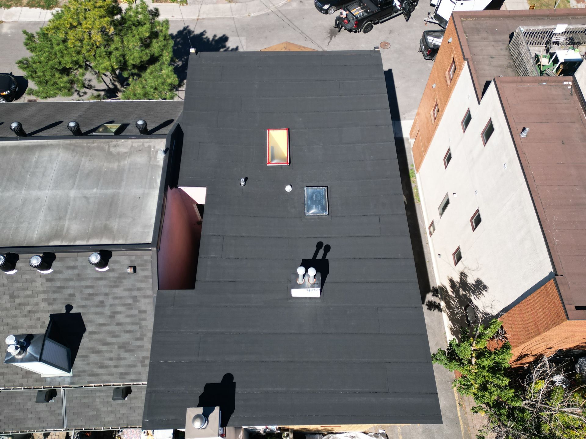 Aerial view of flat black rooftops between buildings, with skylights and rooftop vents.