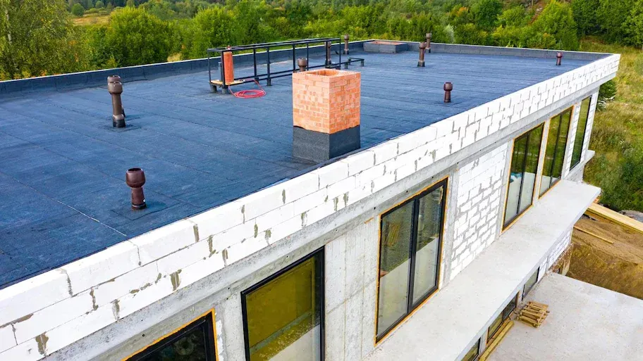 Rooftop with blue waterproof membrane, vents, and a brick chimney on a white building