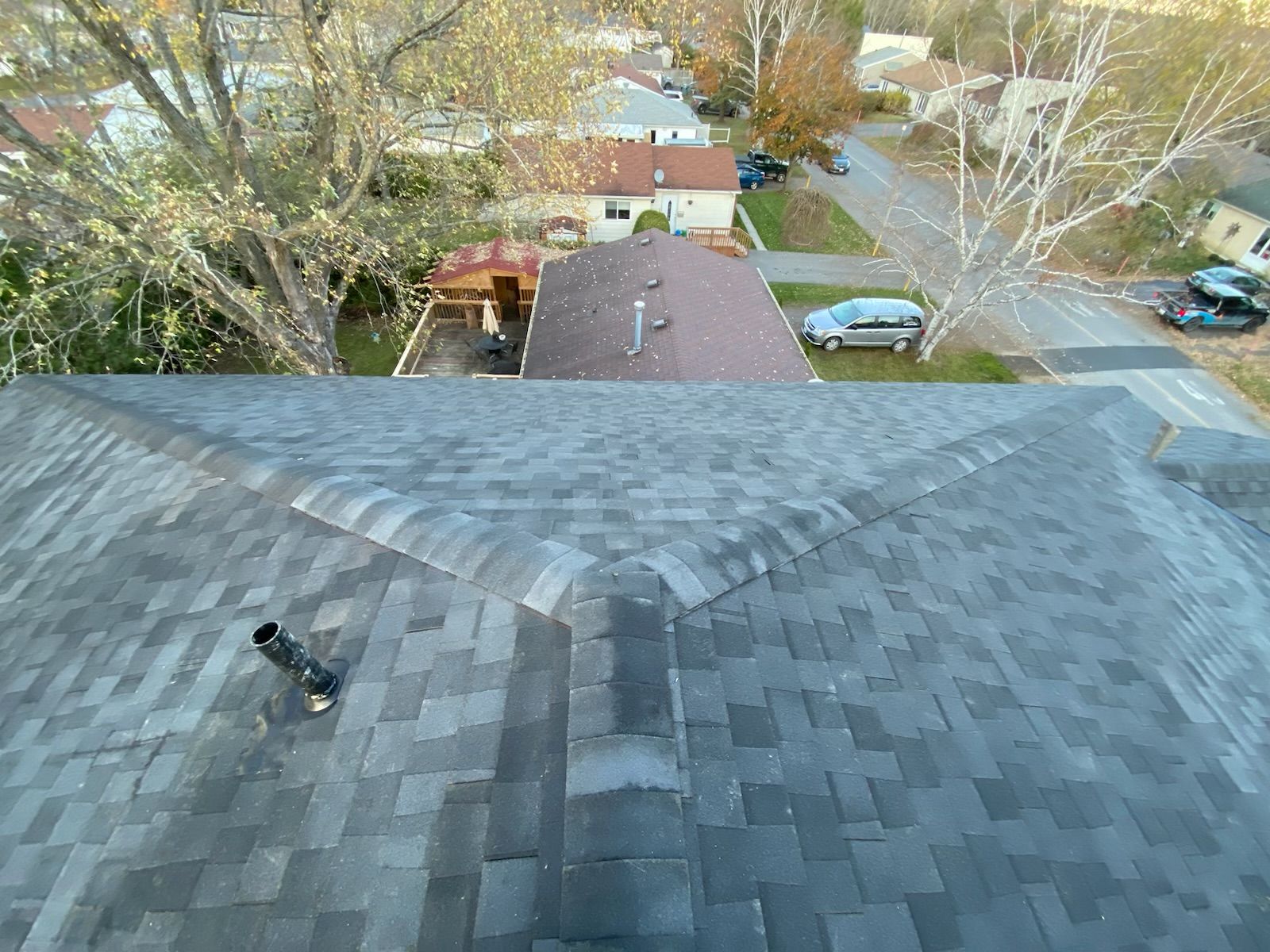 View from a roof ridge over a suburban neighborhood with trees, houses, and parked cars