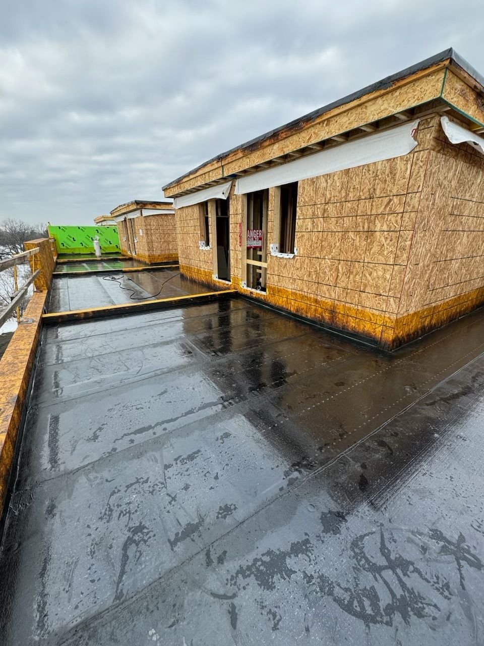 Wet rooftop with black coating, straw-bale walls, and a green tarp in the distance