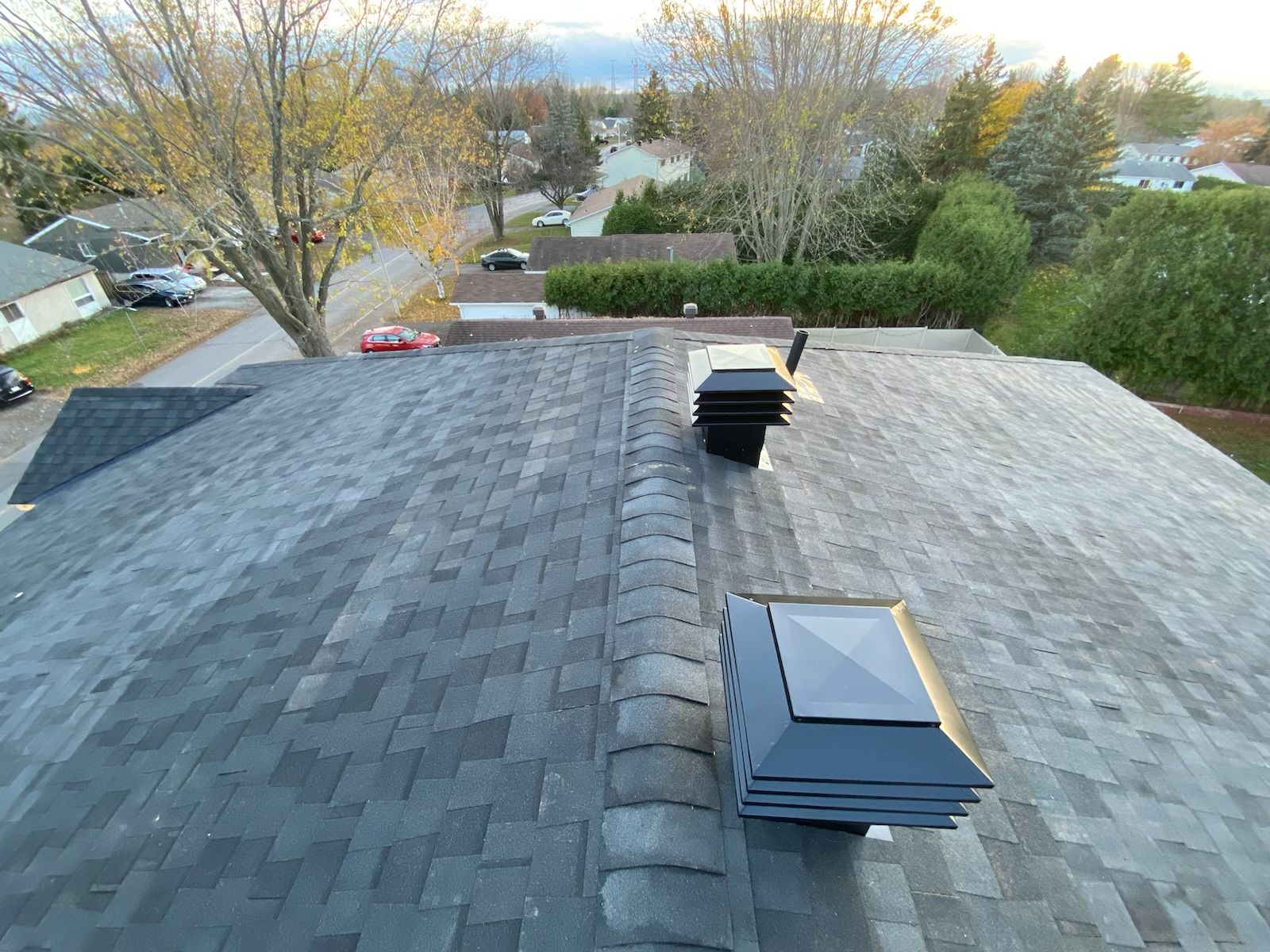 Rooftop shingles with two vents, viewed over a suburban neighborhood at dusk
