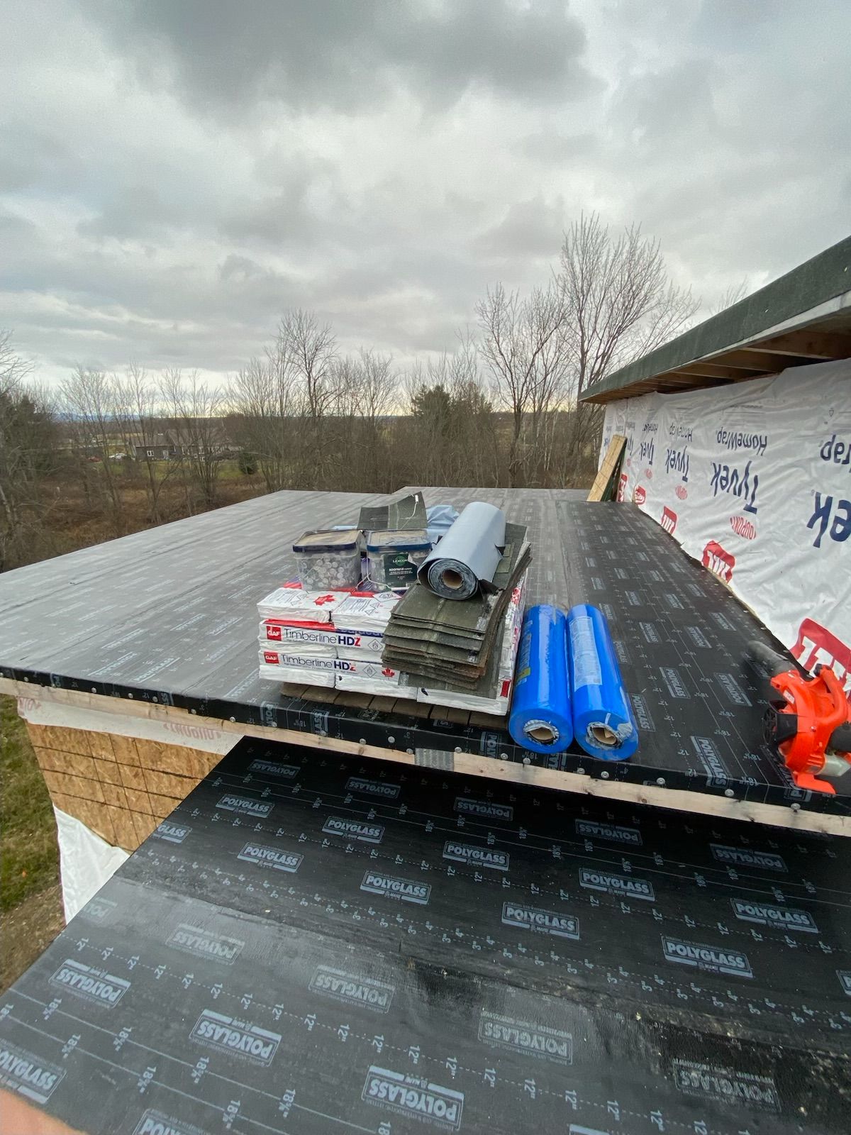 Roof under construction with roofing materials on a black underlayment and cloudy sky in the background