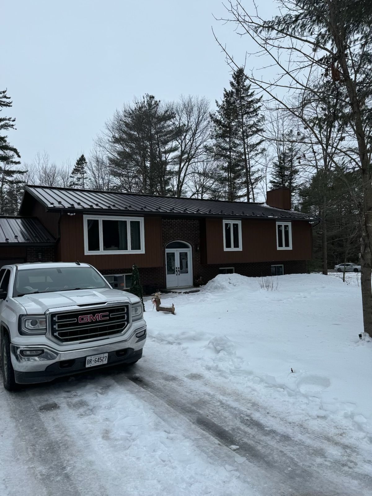 Snow-covered driveway with a dark brown house and a white pickup truck in front.