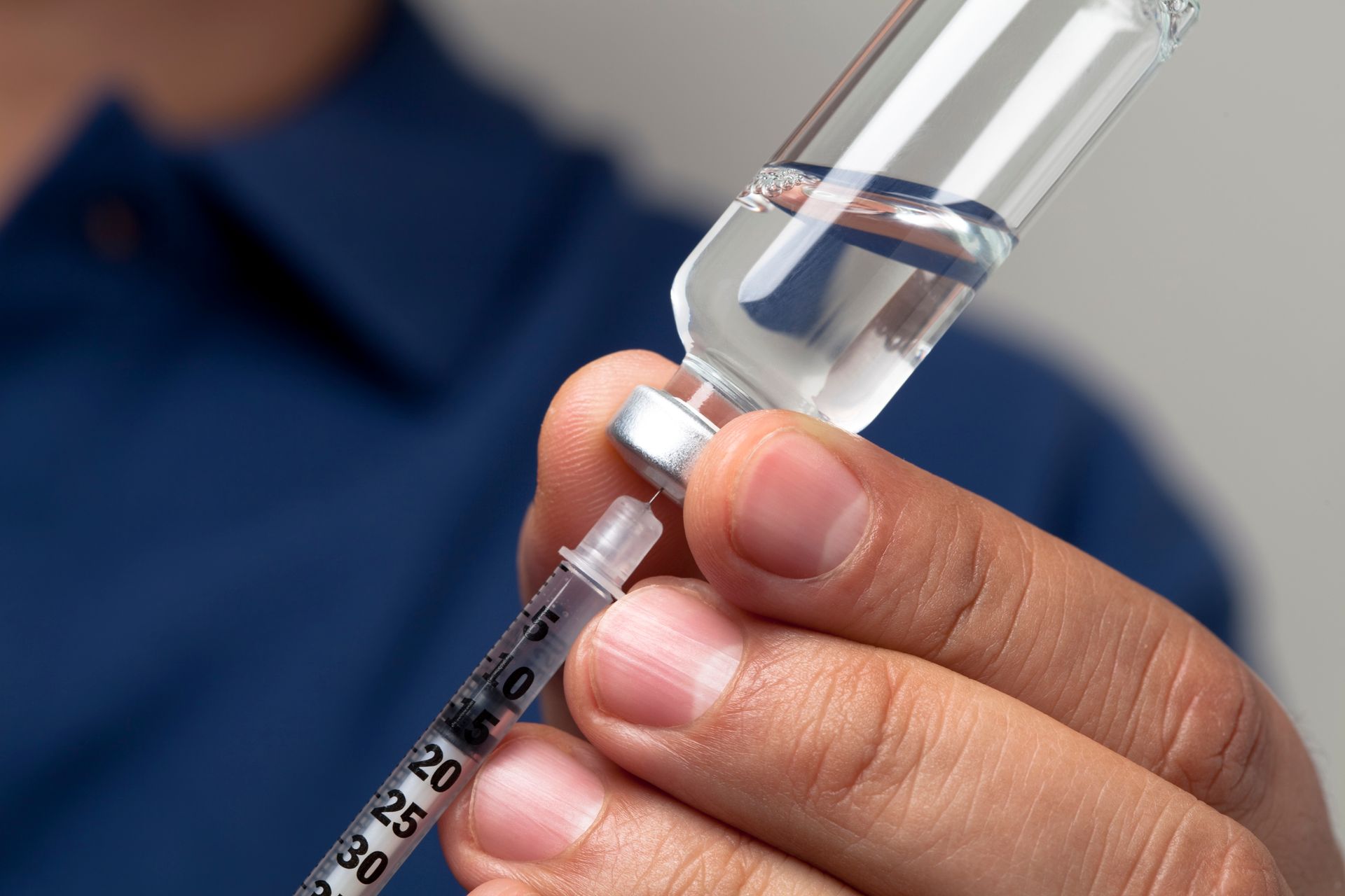 Person drawing medication from a vial with a syringe.
