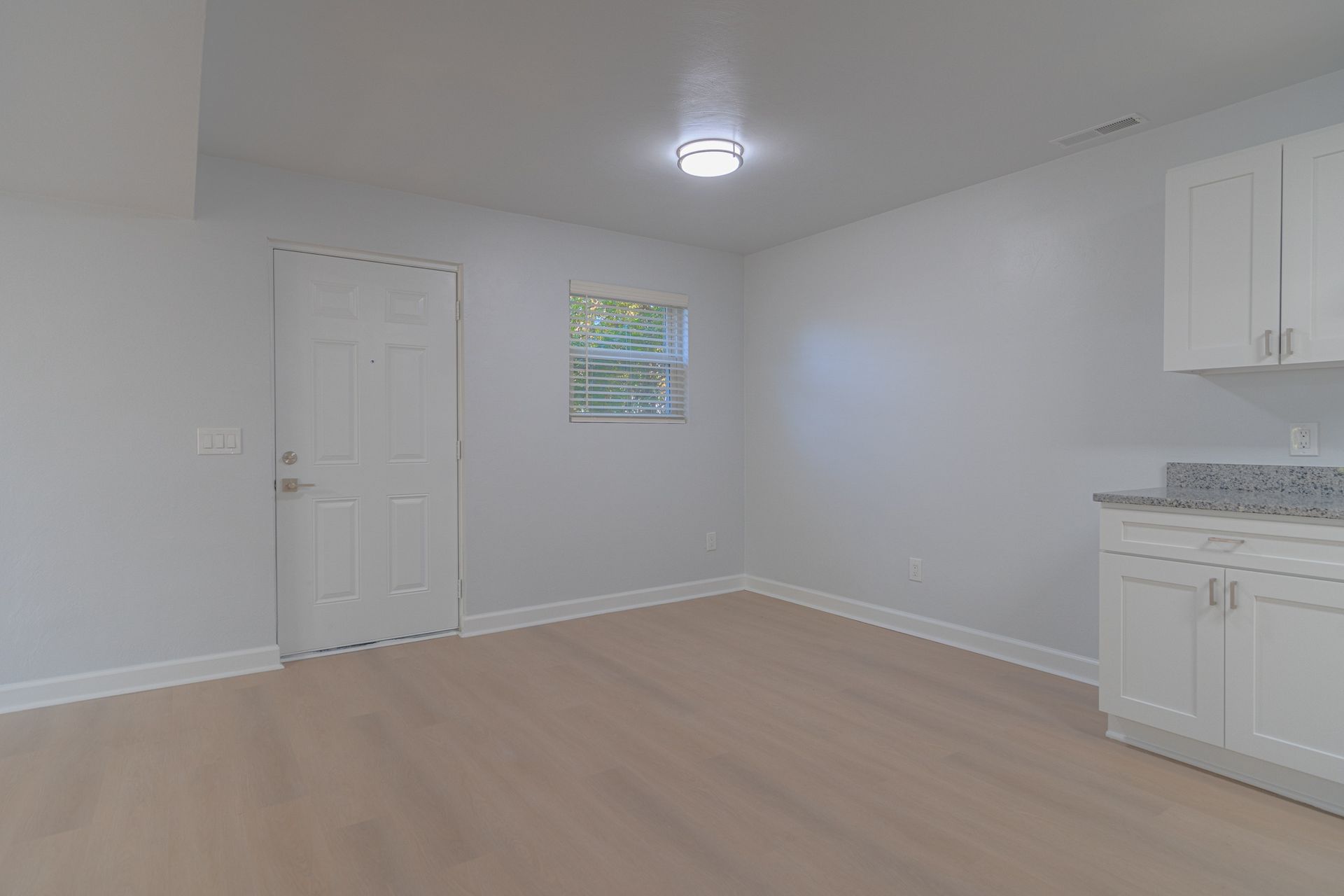 Empty white kitchen and living area with light wood floors, white cabinets, and a ceiling light