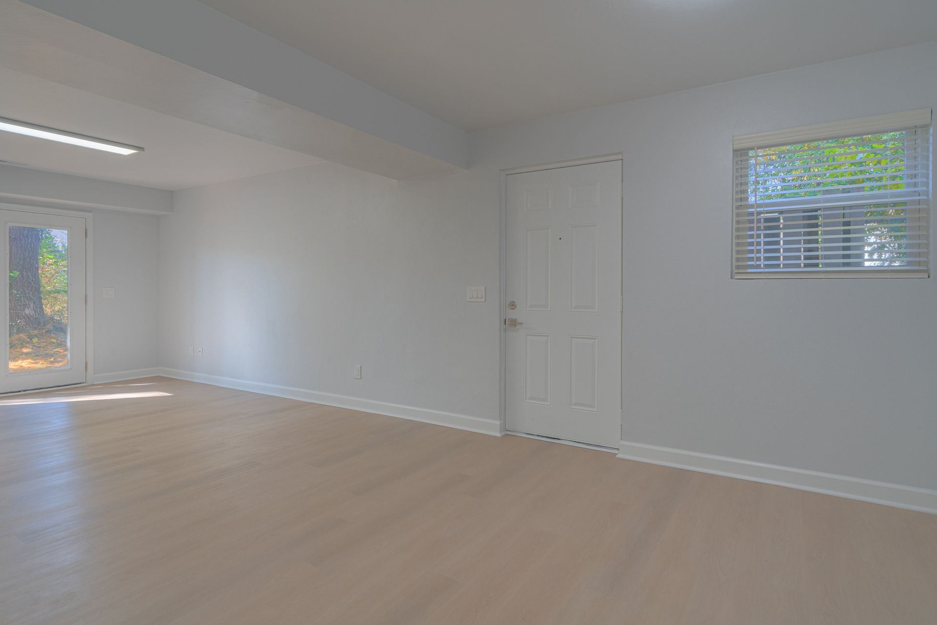 Empty white room with light wood floors, a window, and a closed door.