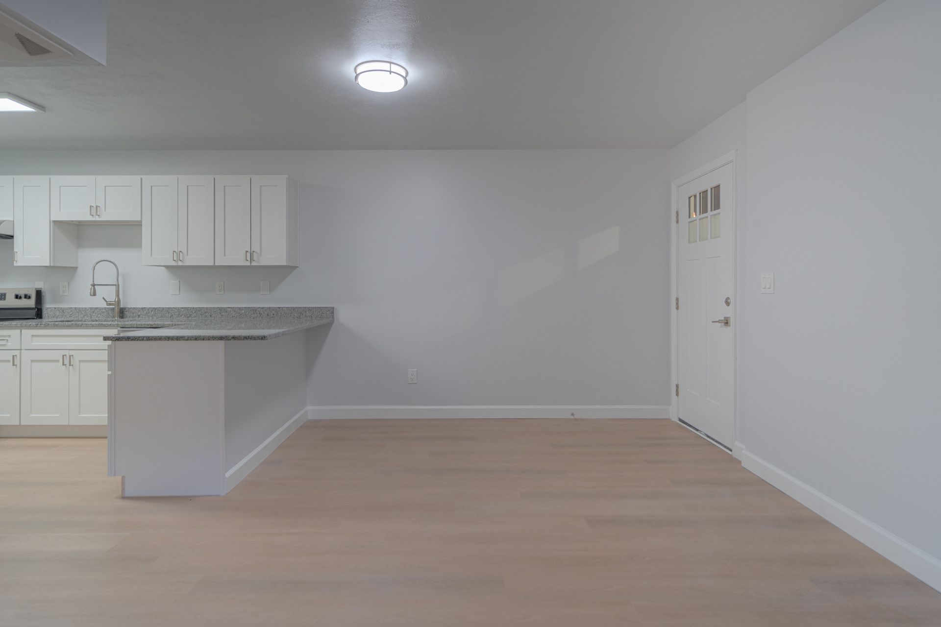 Empty modern apartment living room with kitchen, white walls, and light wood floors