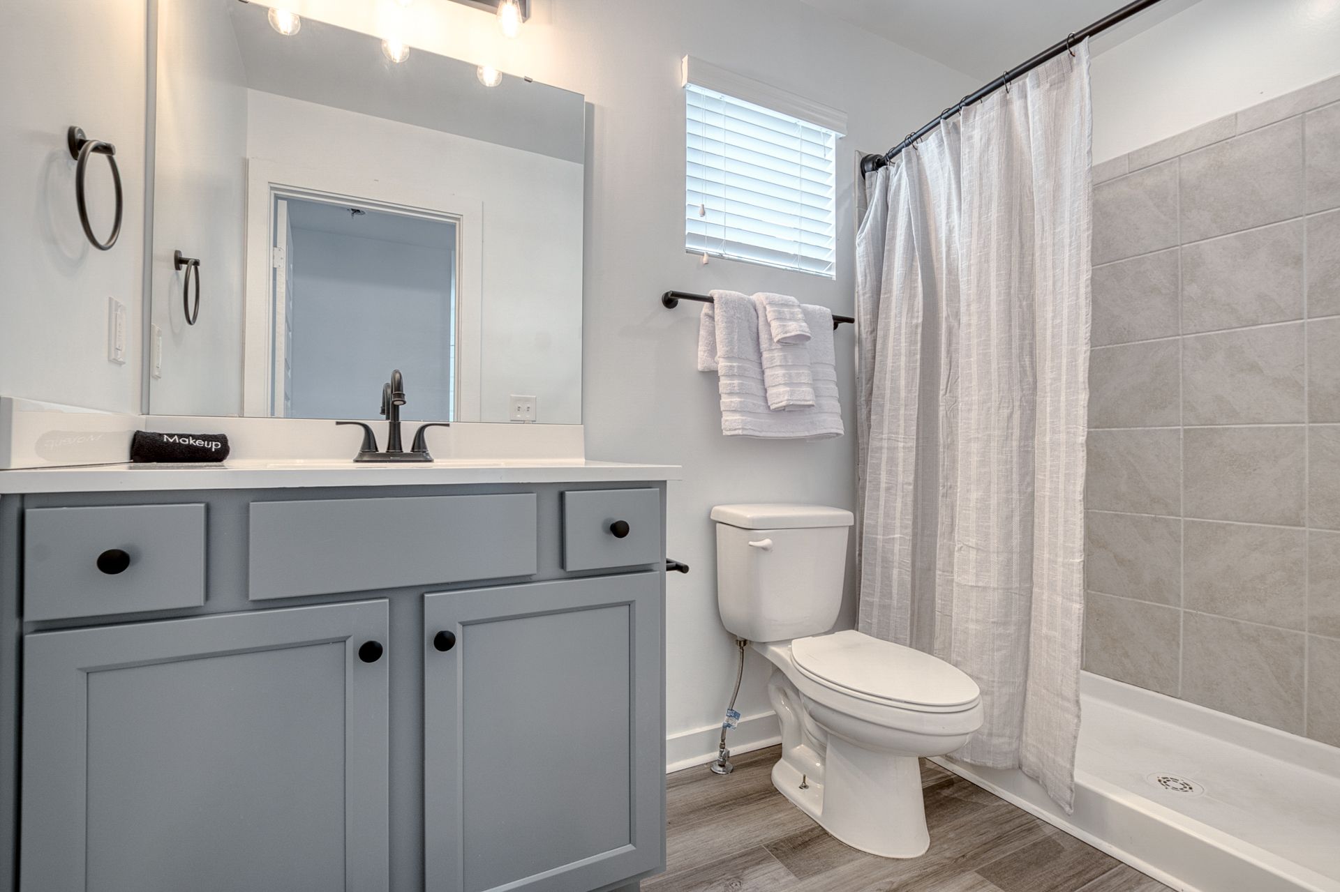 Bright bathroom with gray vanity, toilet, tub, and white shower curtain