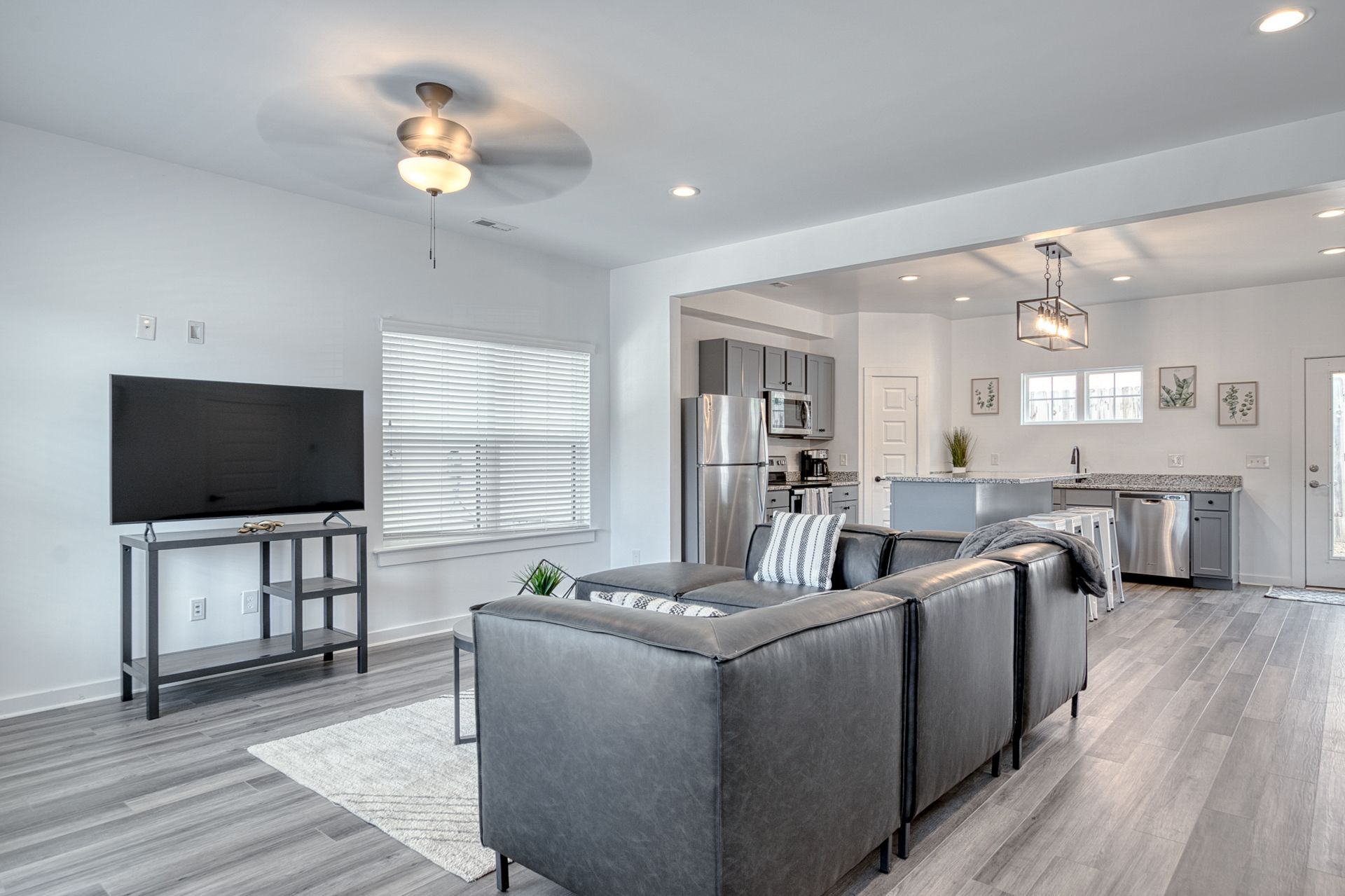 Modern open-concept living room with gray sofas, TV, and kitchen in the background