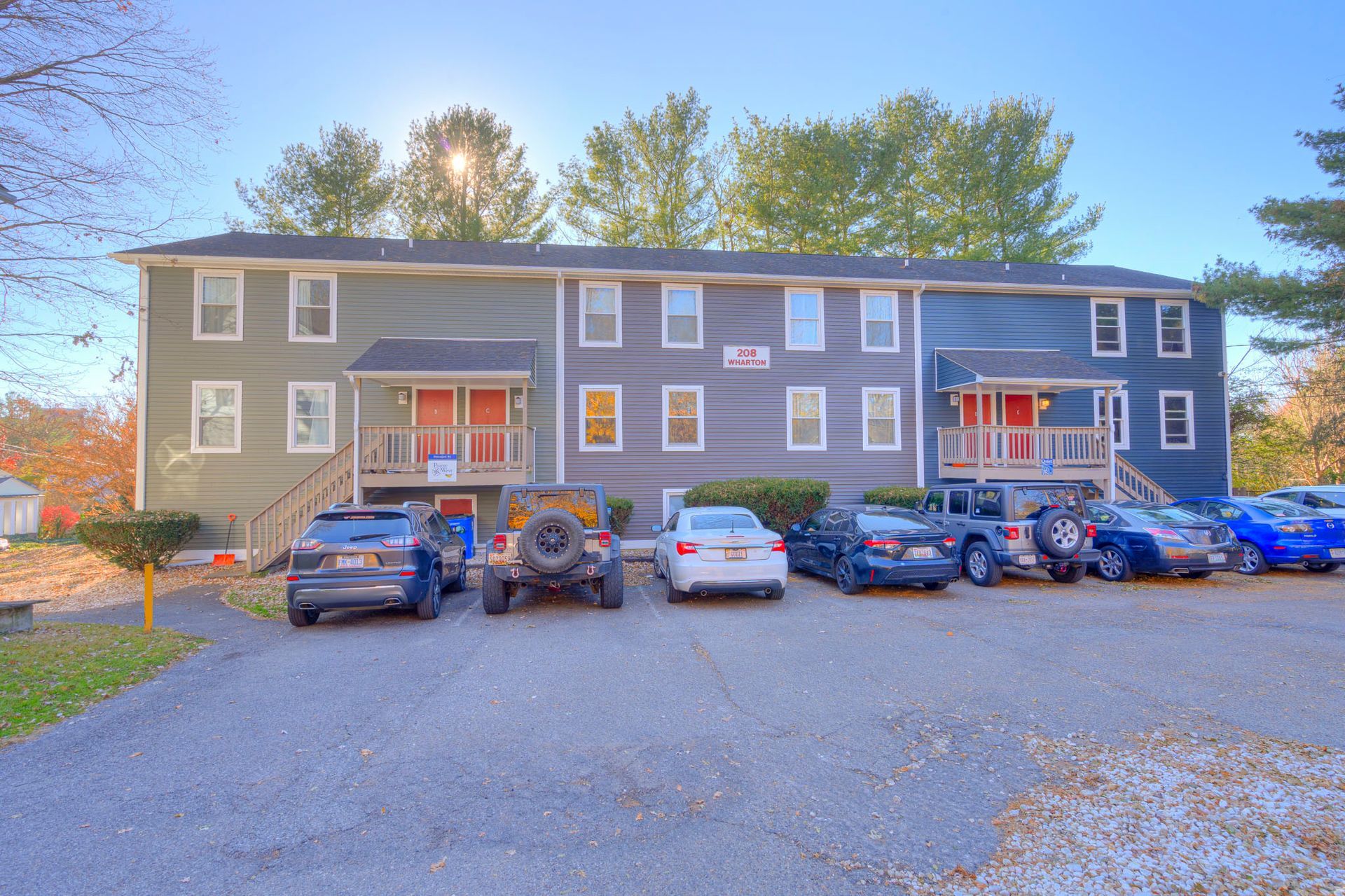 Two-story apartment building with parked cars in a gravel lot at dusk