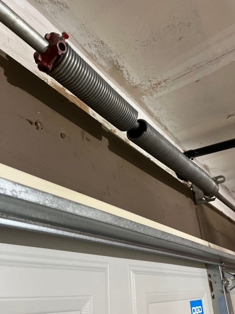 Garage door torsion spring and metal track mounted above a white door.