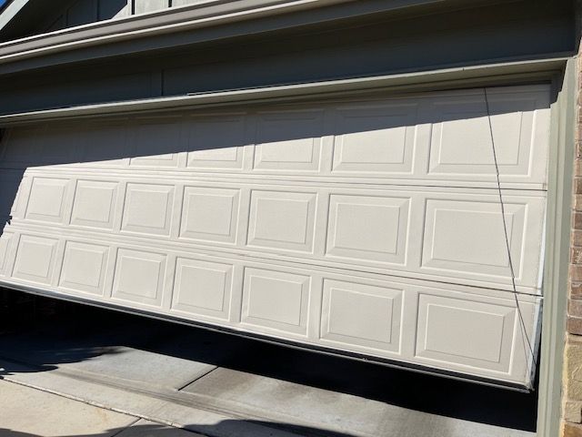 Partially open white garage door with rectangular panels, revealing a dark interior