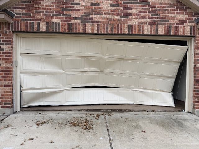 Dented beige garage door bent inward on a brick house driveway.