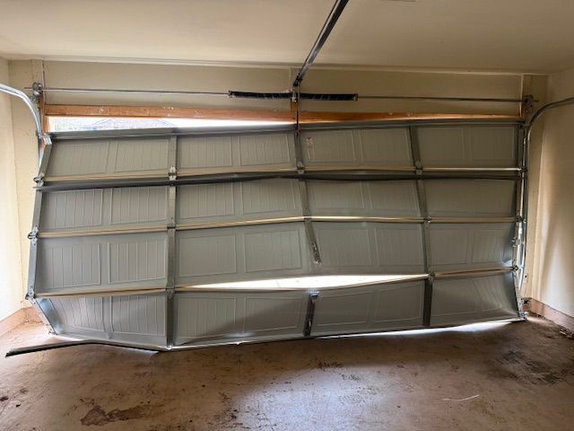 Damaged garage door bent inward with panels buckled and bottom edge hanging loose